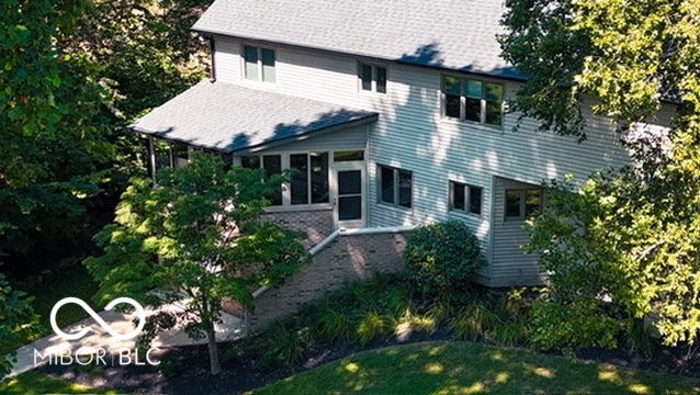 Two-story light blue-gray house with a covered entrance, surrounded by mature trees and landscaping.