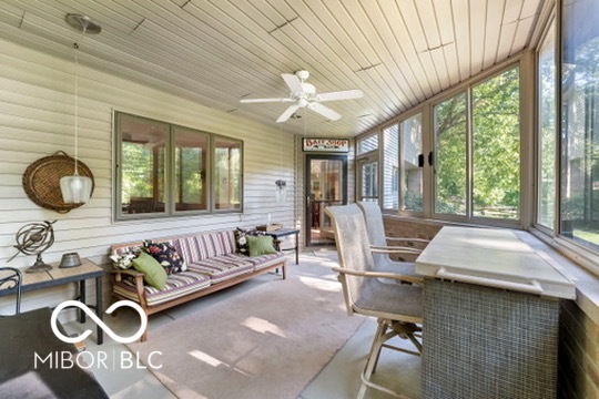 Enclosed sunroom with a striped sofa, wicker dining table, and large windows overlooking greenery.