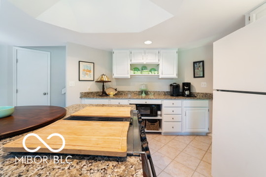 Kitchen with white cabinets, granite counters, tiled floor, and a large wooden island table.