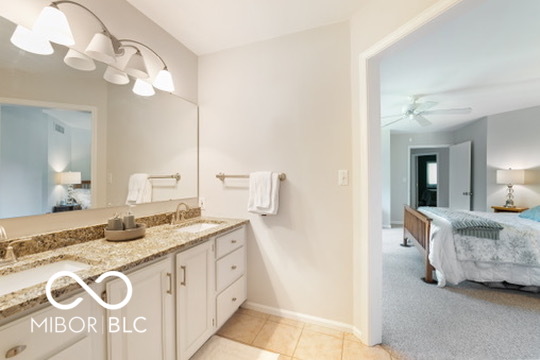 Bathroom vanity with granite counter and mirror, looking through an open doorway into a furnished bedroom.