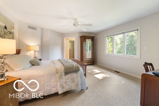 Furnished bedroom with a quilted bed, wooden wardrobe, and large sunlit windows.