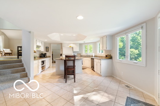 Bright kitchen with a central island, tiled floor, and large windows overlooking greenery.