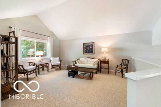 Living room with vaulted ceiling, beige carpet, and seating beside a large window.