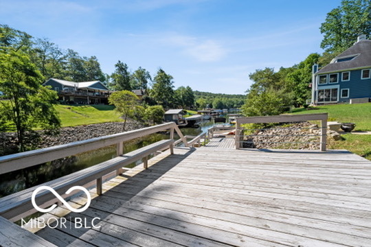 Wooden lakeside dock with railings, calm water, and tree-lined shores with homes.