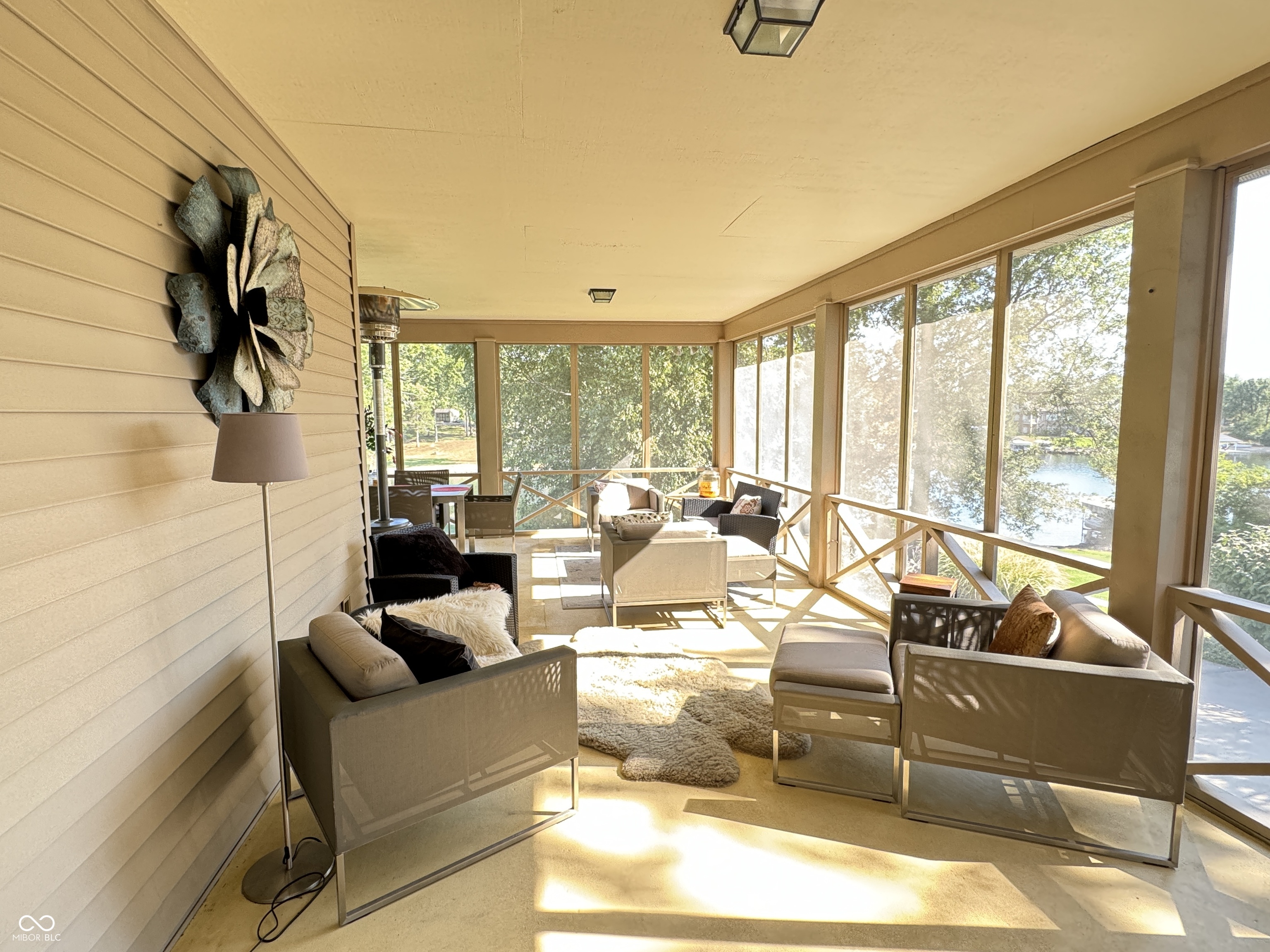 Furnished sunroom with beige seating and large windows overlooking a lake.