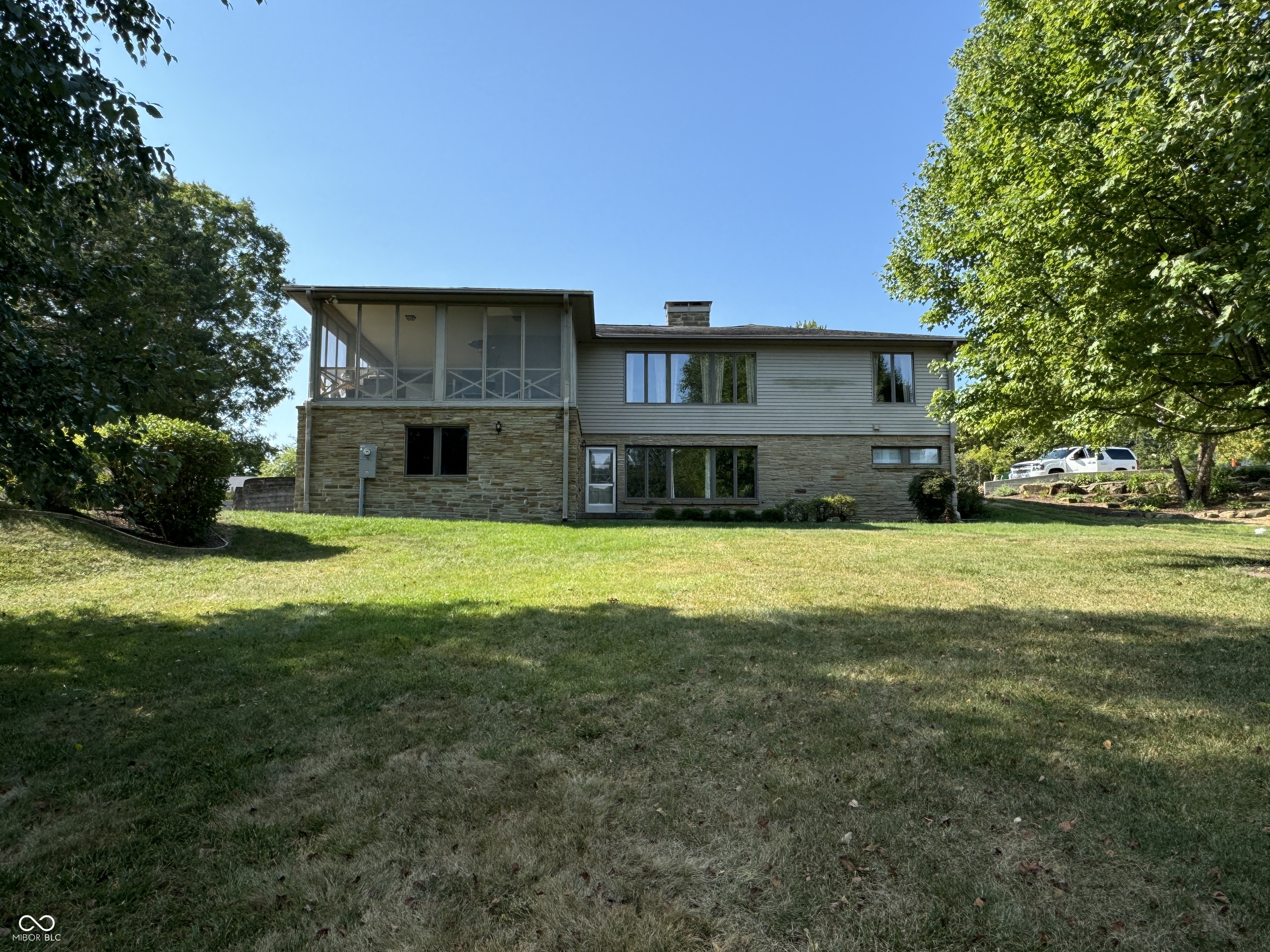 Home with stone lower level and elevated screened porch, viewed across a sloping lawn.