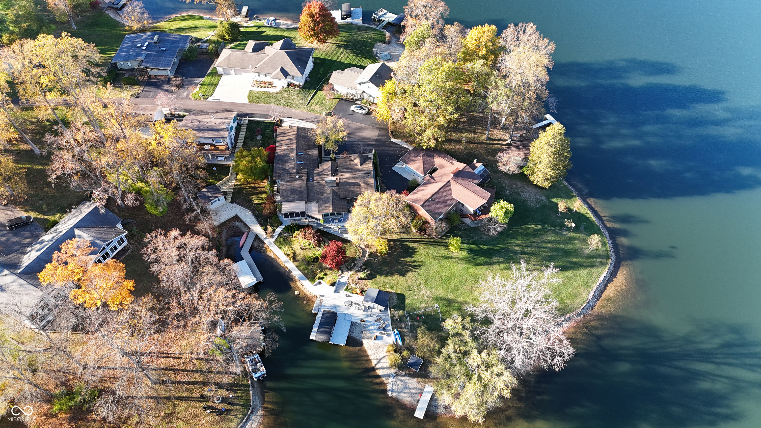 Aerial view of a lakefront property with docks, a curved shoreline, and autumn trees.