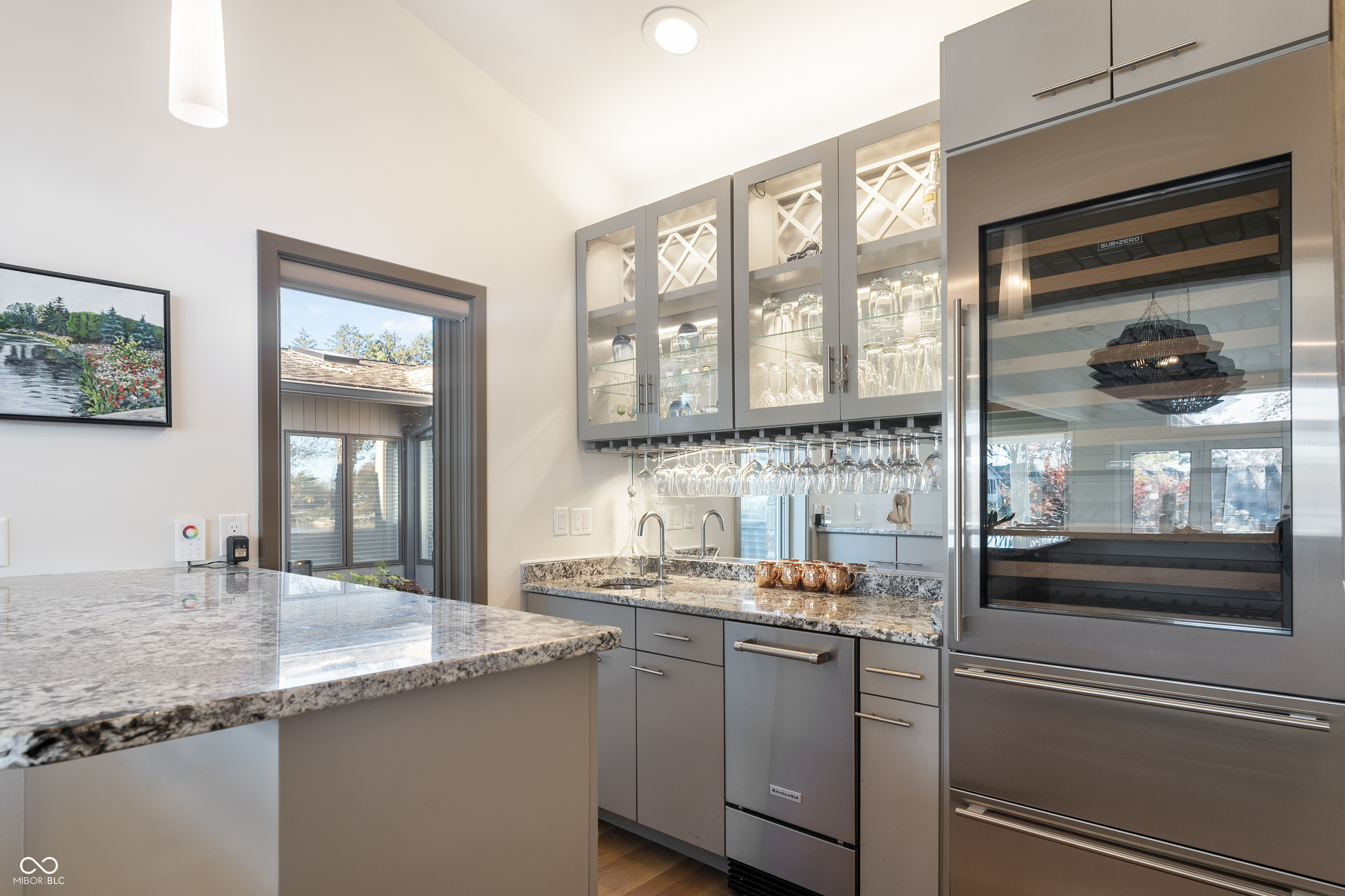 Kitchen bar with glass-front stemware cabinets, hanging wine glasses, stone counters, and a built-in wine refrigerator.