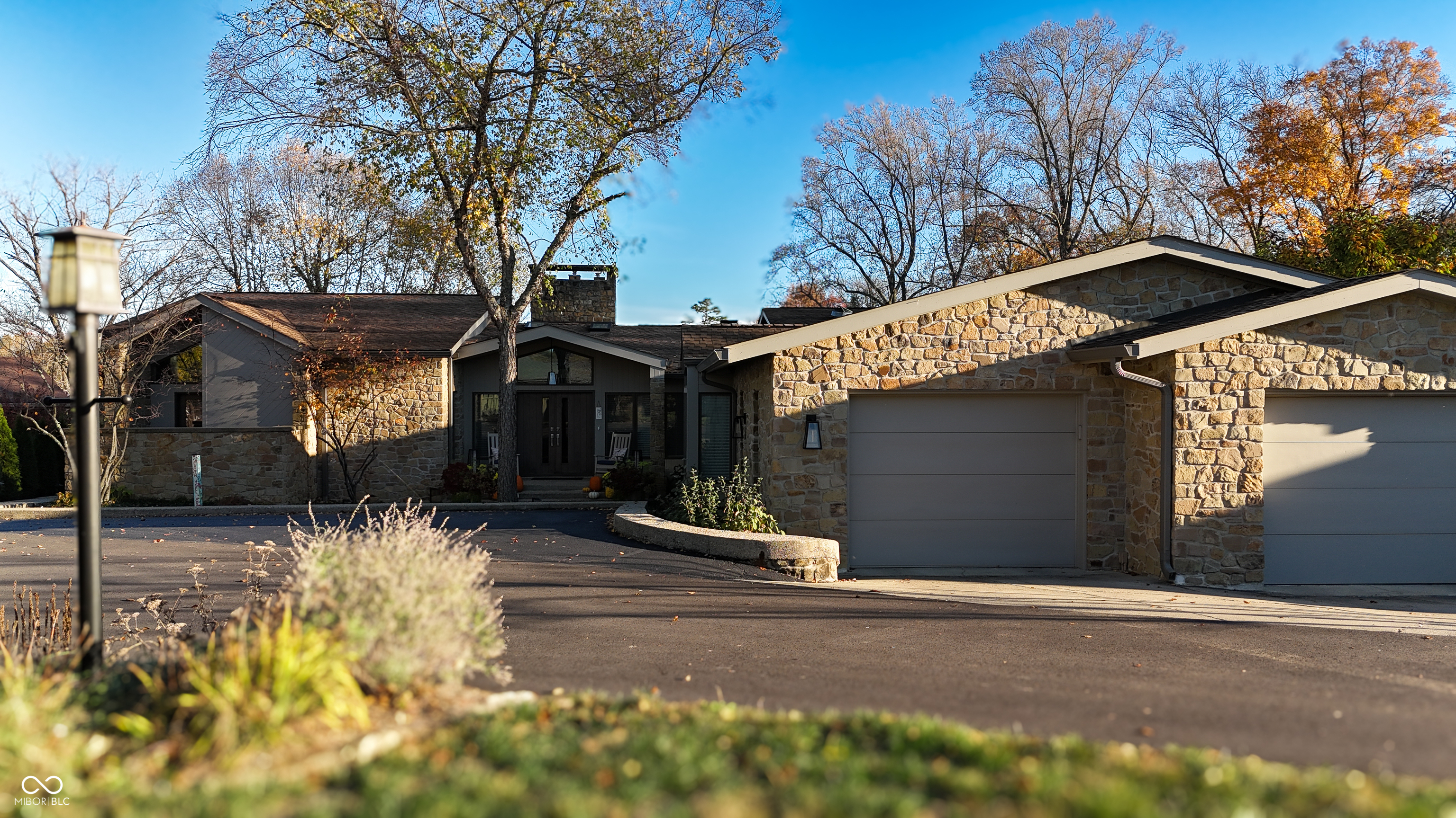 Stone house exterior with two attached garages, a curved driveway, and mature autumn trees.
