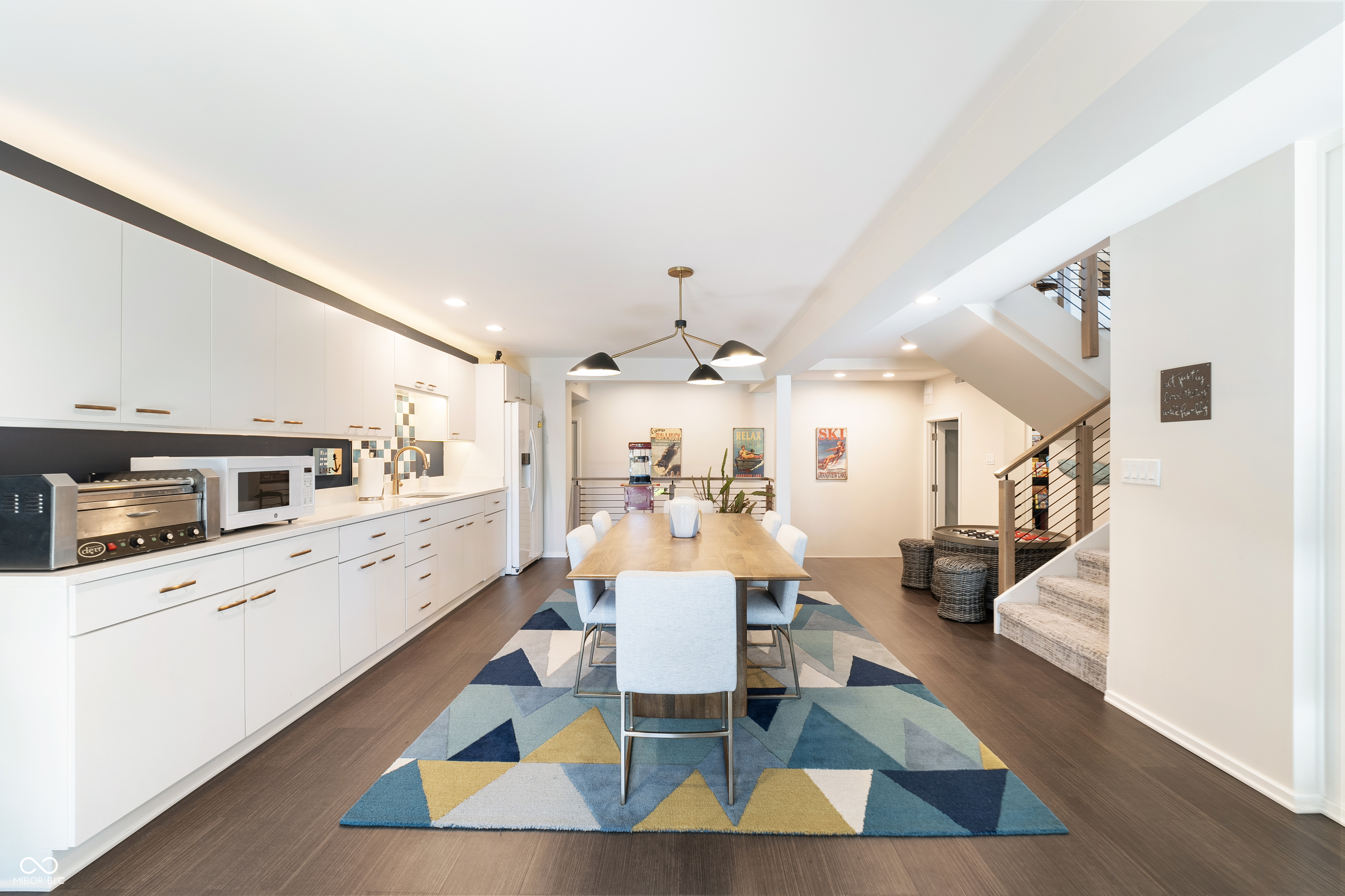 Open-plan kitchen and dining area with white cabinets, a wooden table, and a colorful geometric rug.