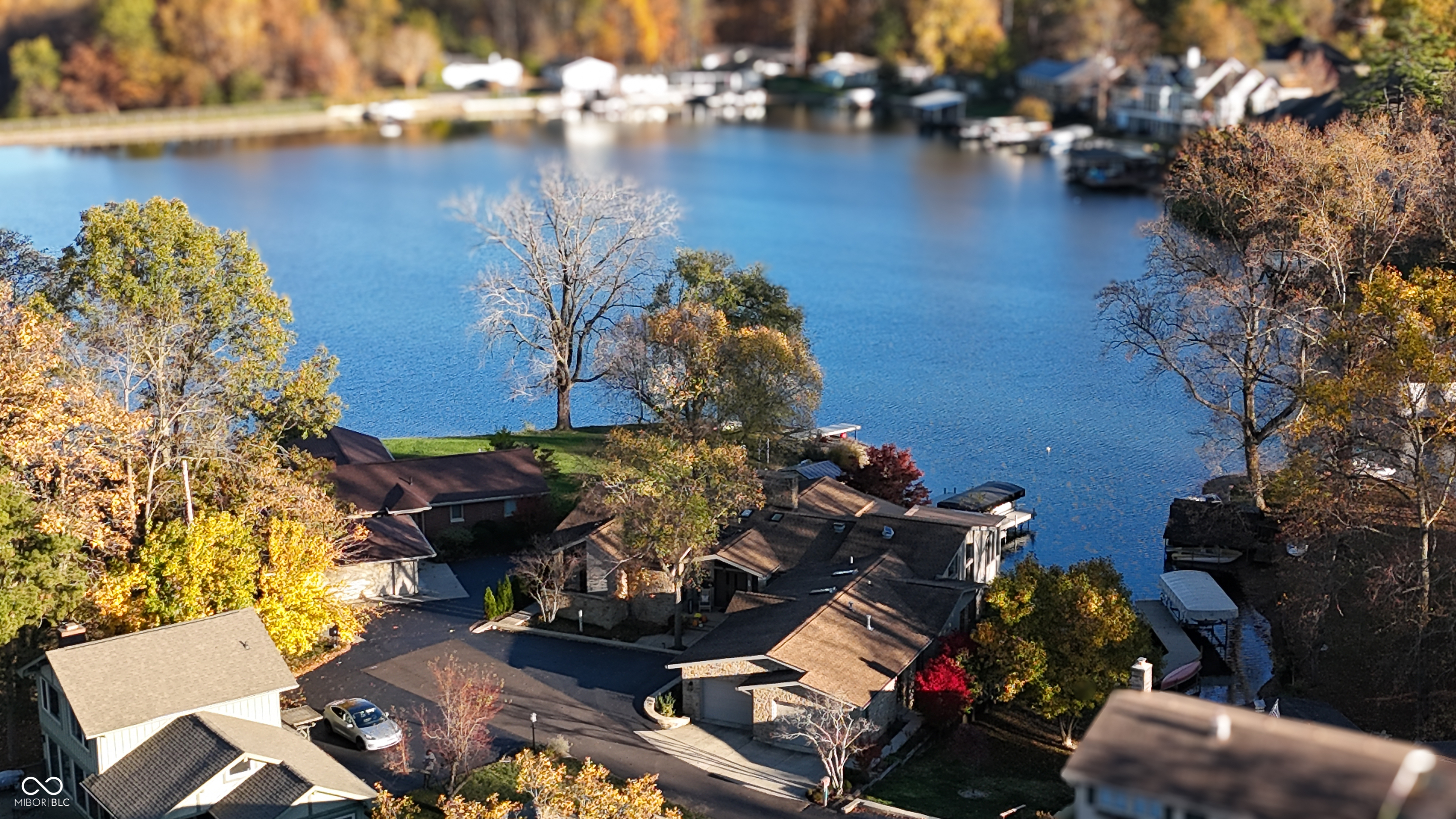 Aerial view of a lakefront home with a dock and autumn trees.