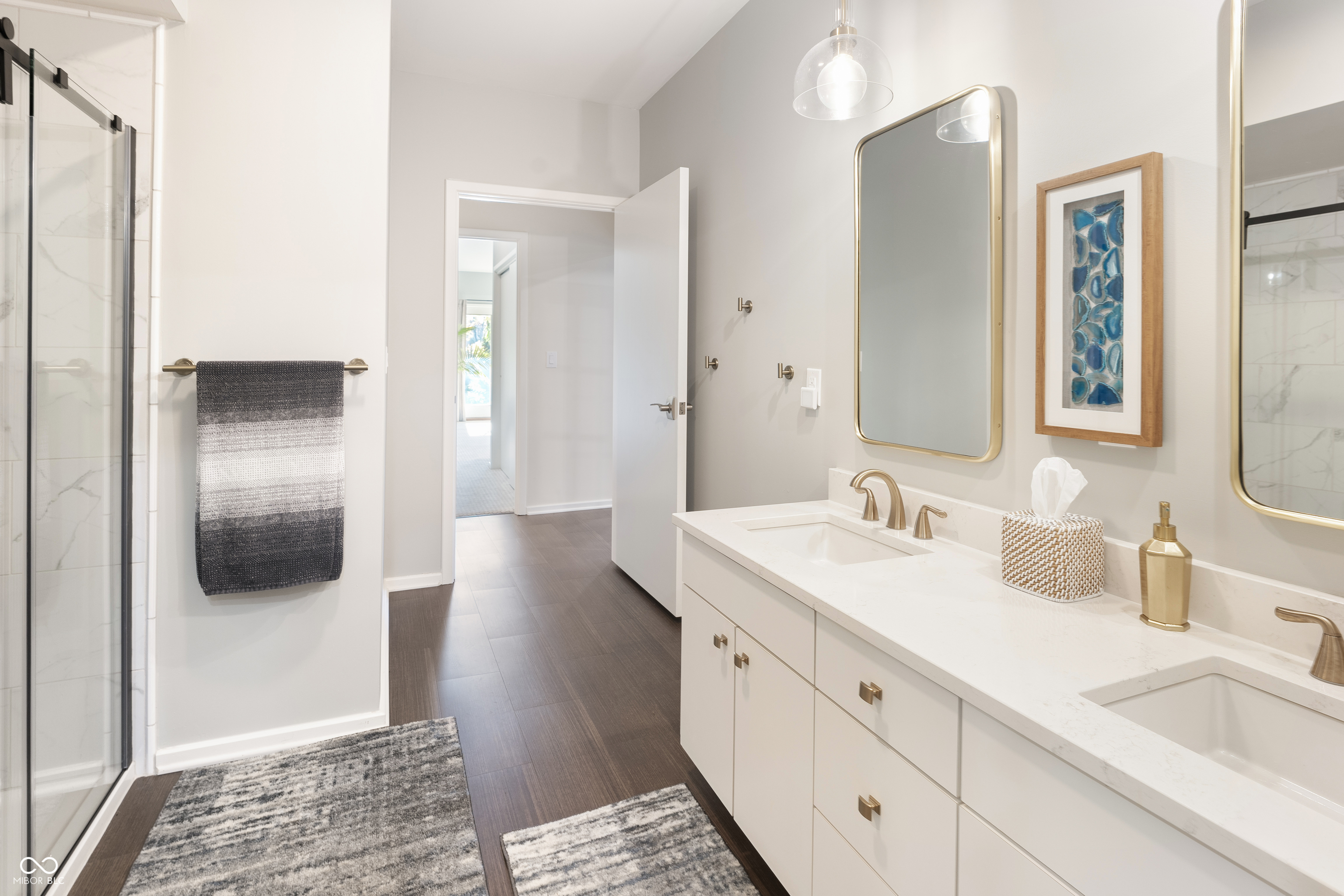 Bathroom with a long double vanity, gold-tone faucets, framed mirrors, and a glass-enclosed shower.