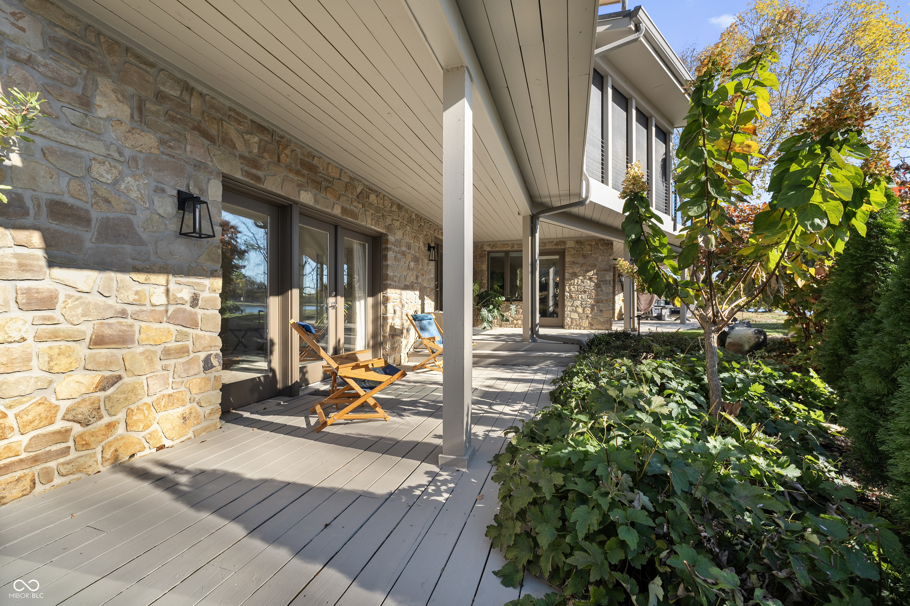 Covered deck with stone walls, folding lounge chairs, and leafy autumn landscaping.
