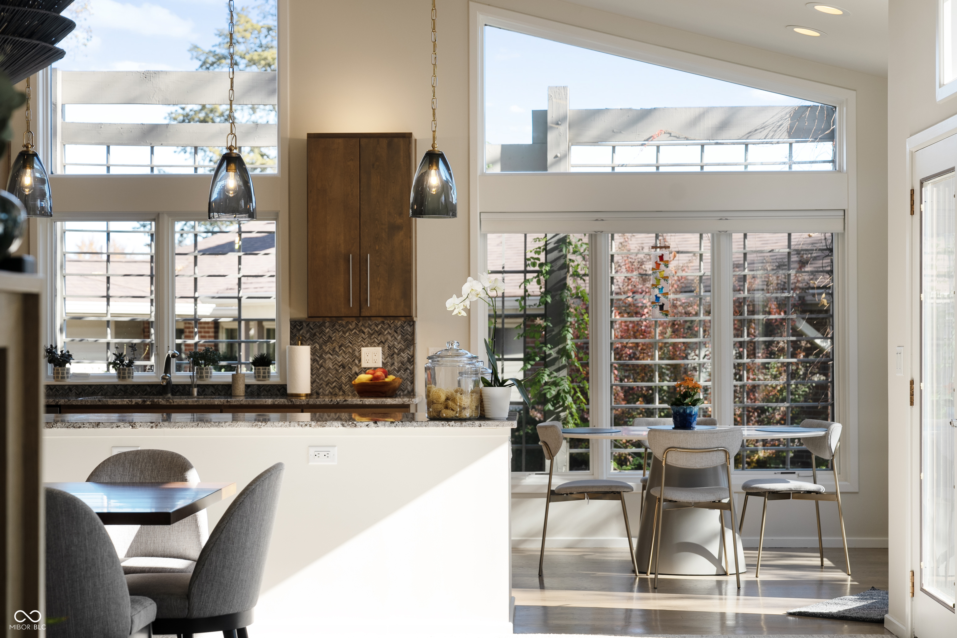 Bright kitchen and dining area with a breakfast bar, dark wood cabinets, and large sunlit windows.