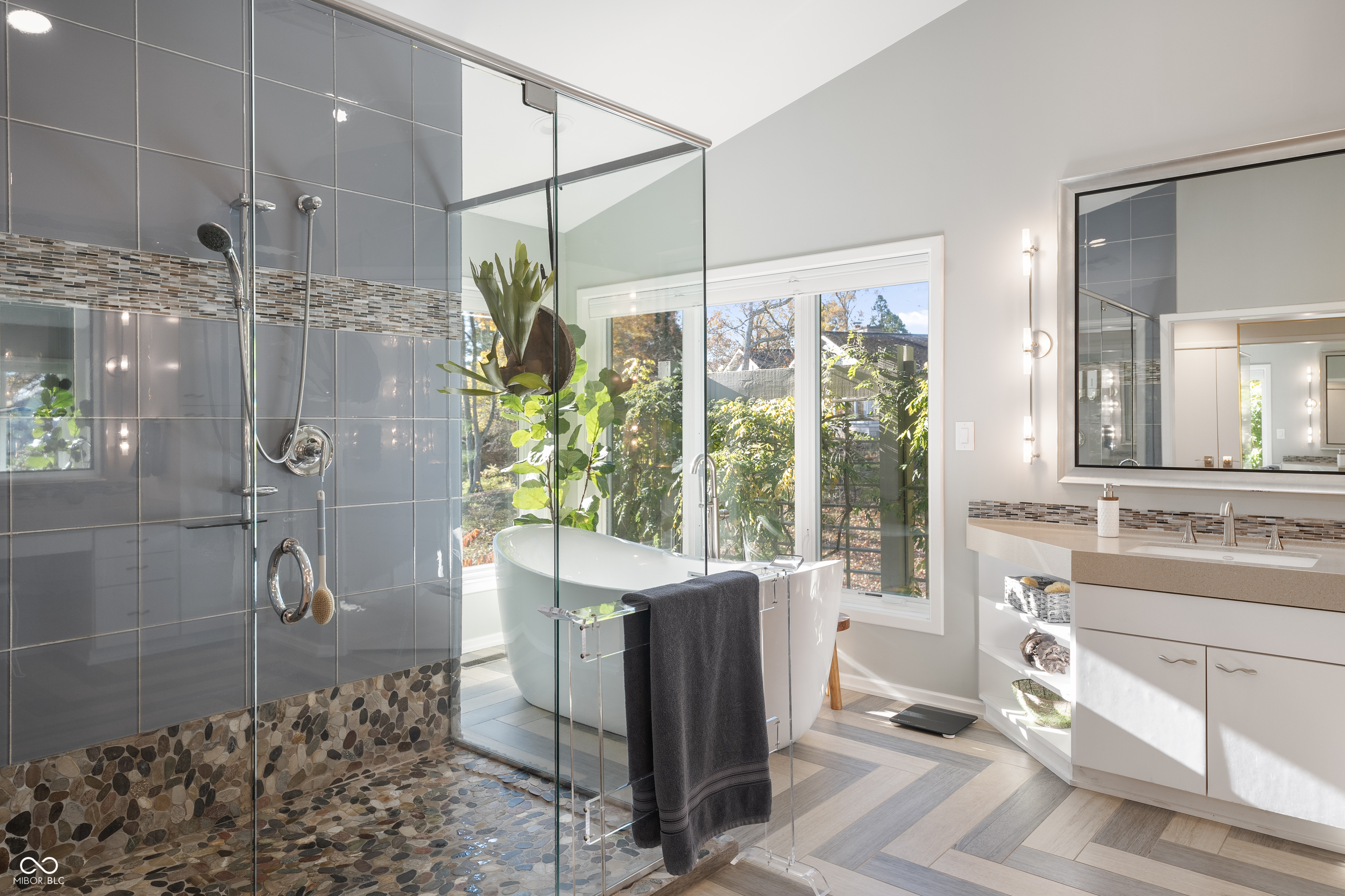 Bathroom with a glass shower, freestanding tub beside a large window, and double-sink vanity.
