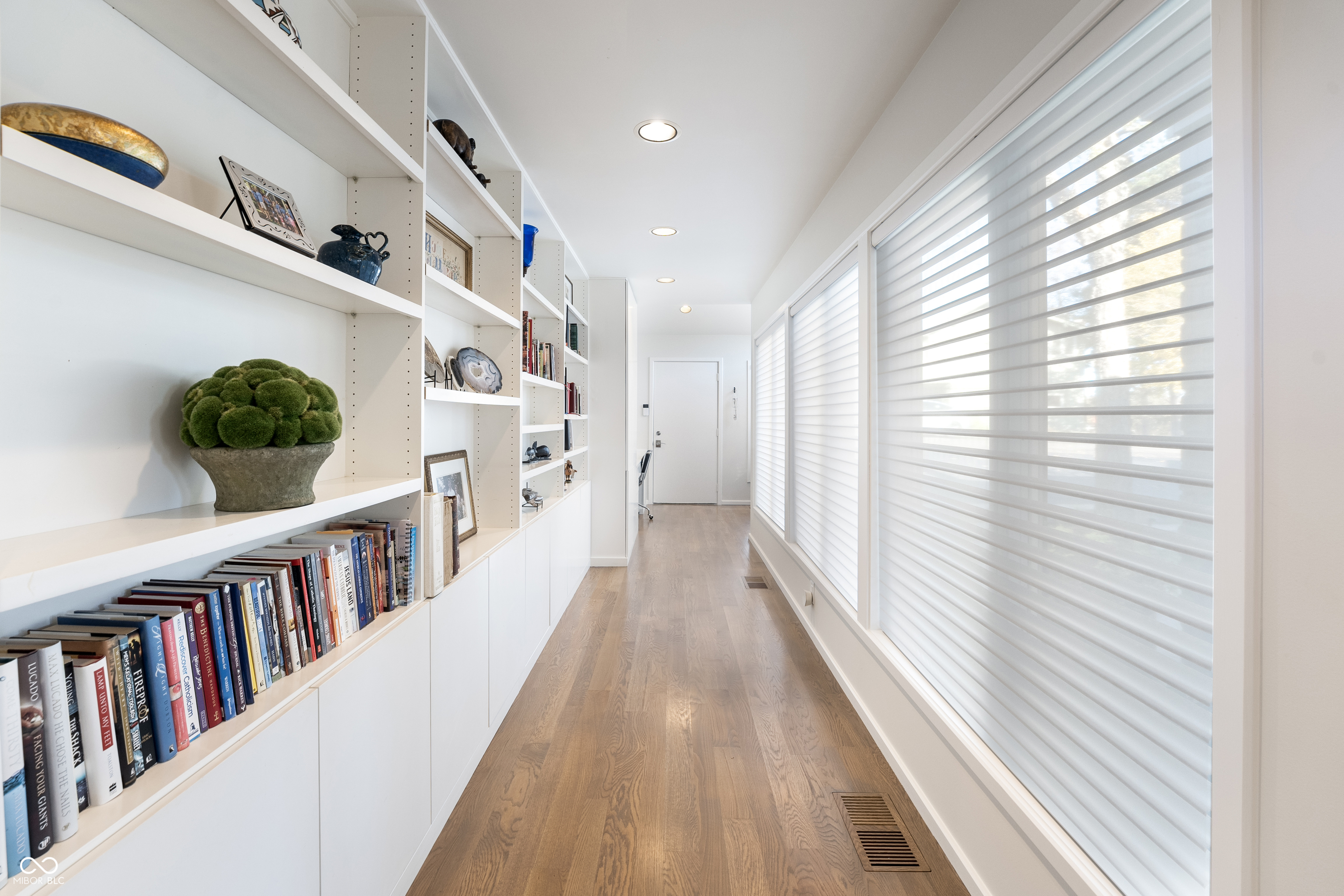 Bright hallway with built-in bookshelves, window blinds, and warm wood flooring.