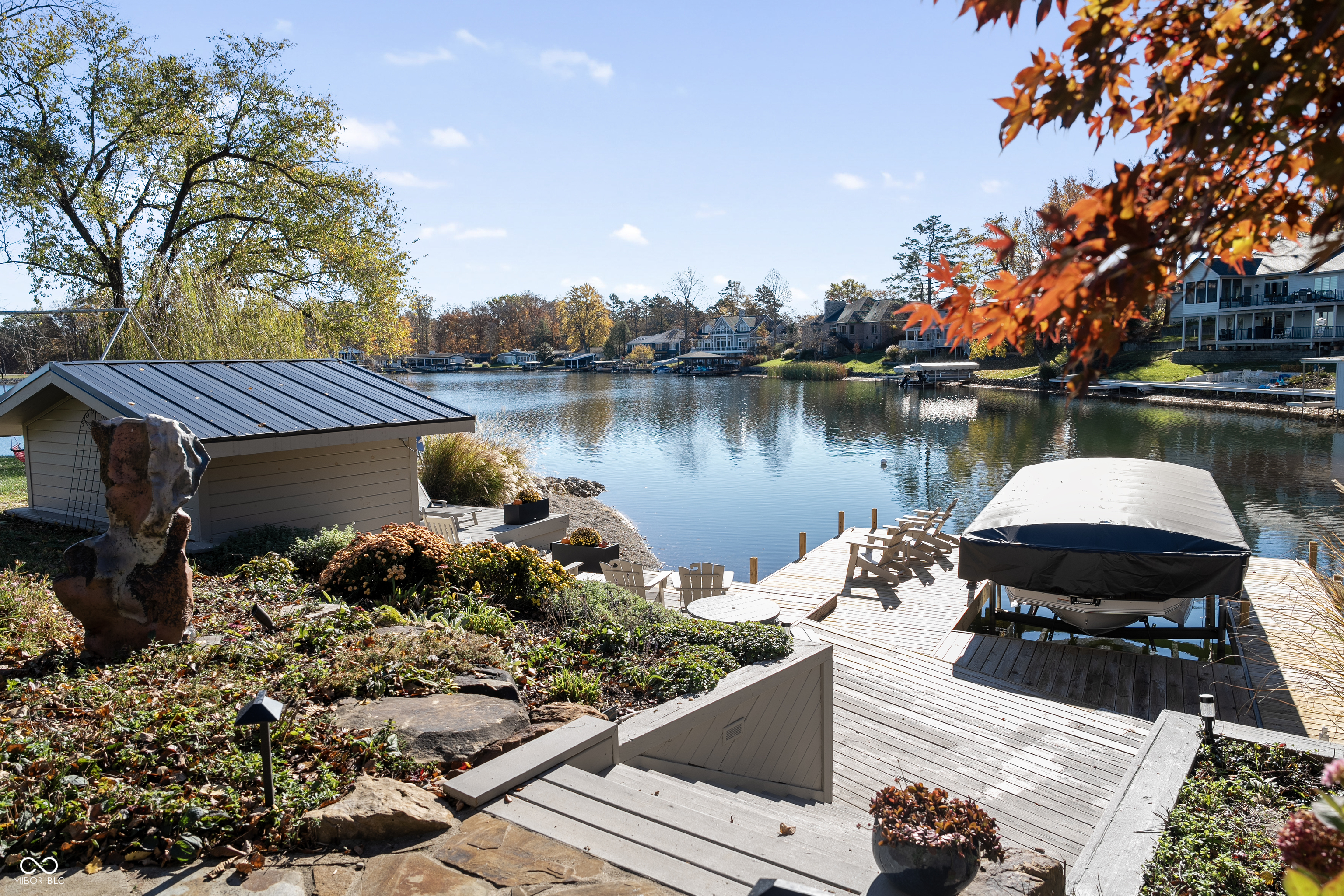 Waterfront dock with a covered boat, seating, and a small boathouse beside a lake.