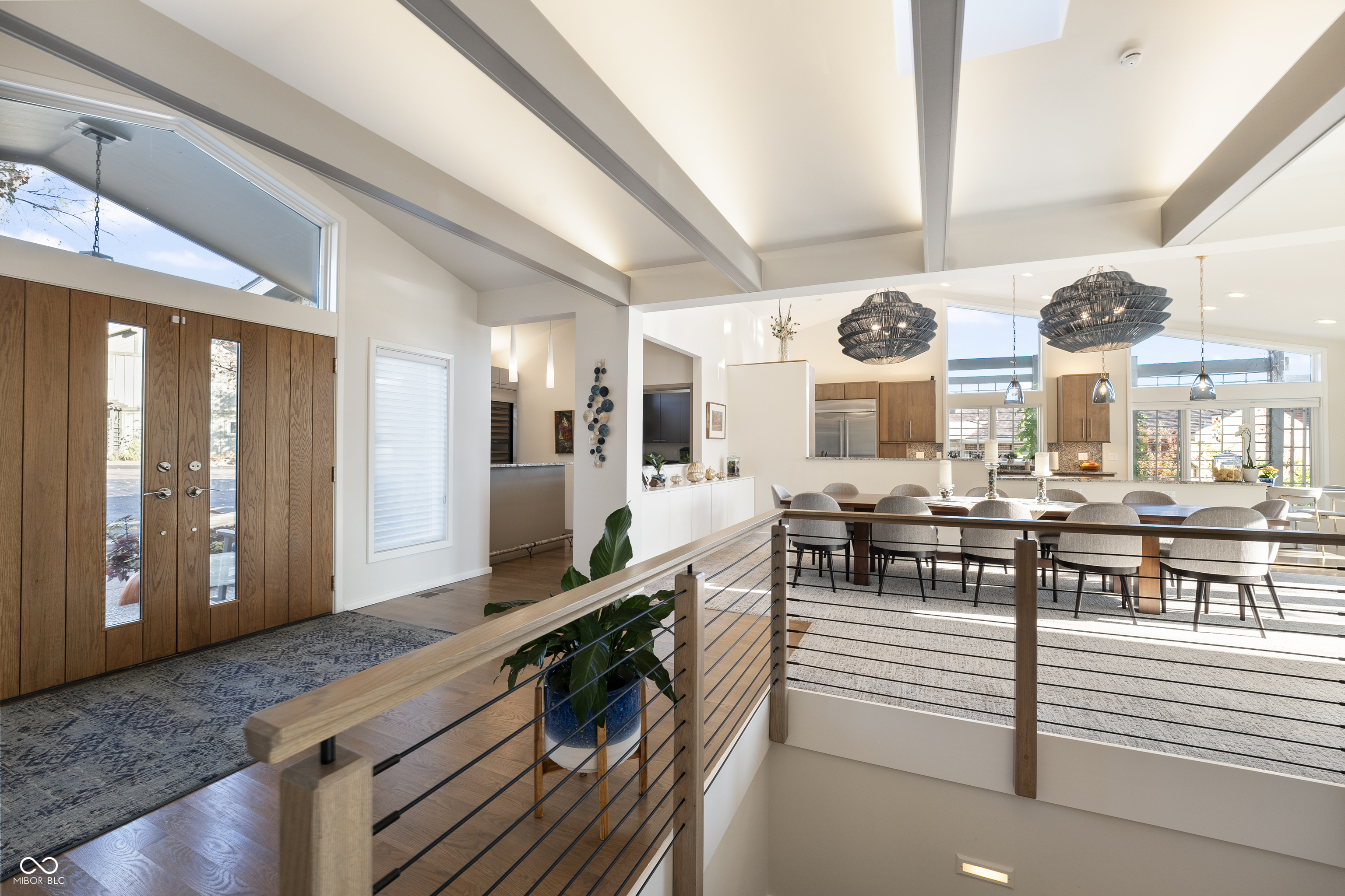 Foyer opening to a dining area, with wood double doors, exposed ceiling beams, and cable railing.