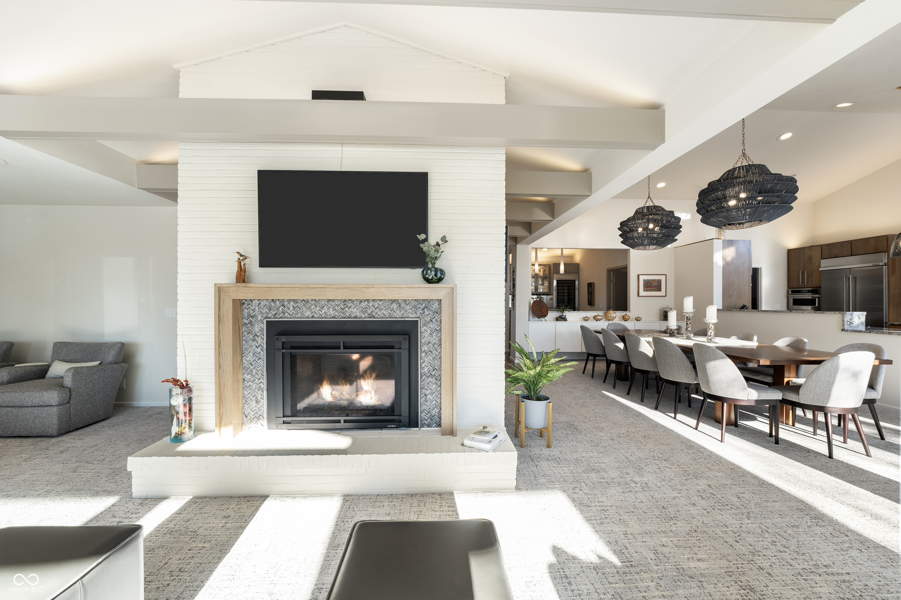 Open-plan living and dining room with a white brick fireplace, long dining table, and sculptural pendant lights.