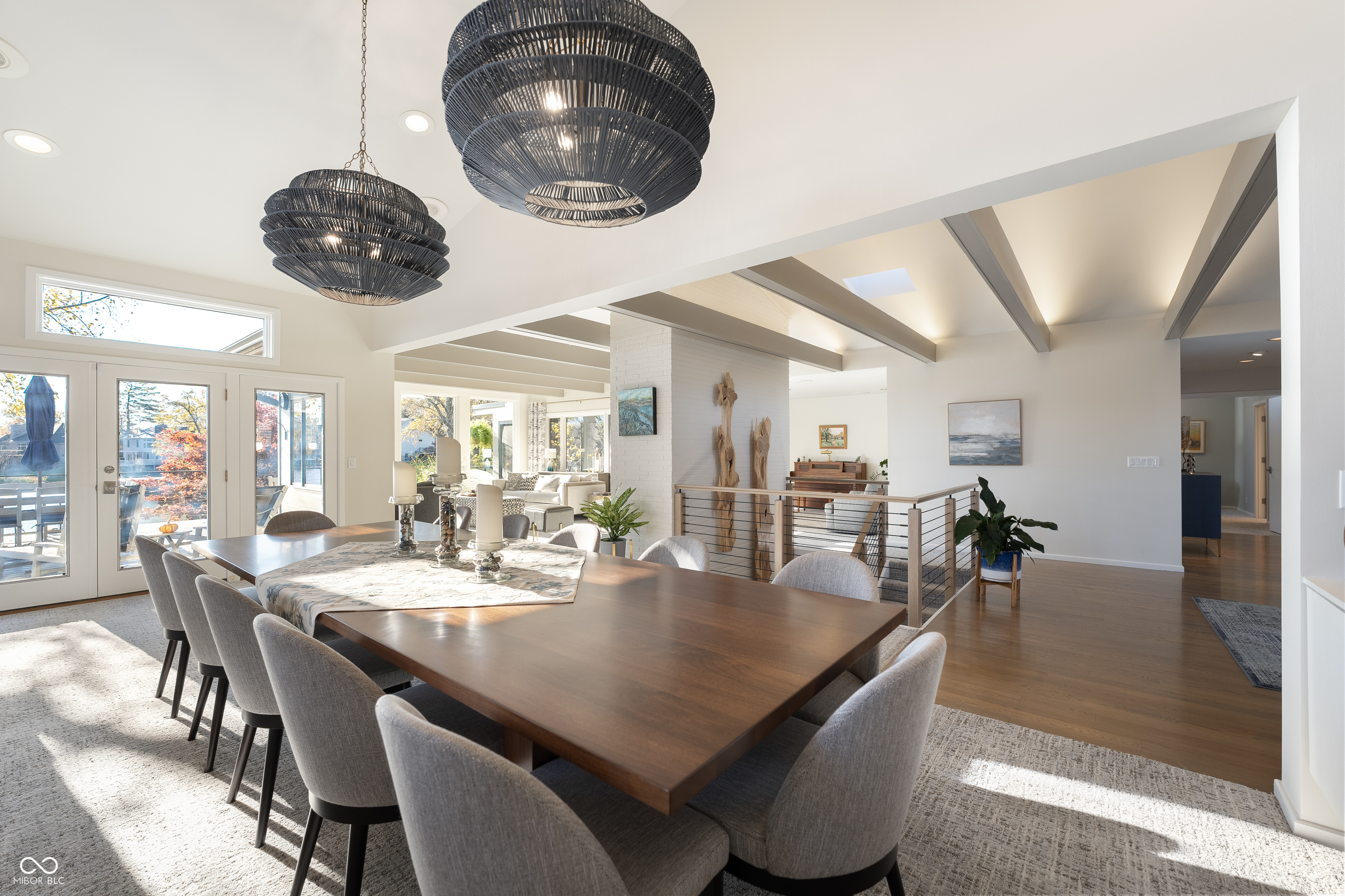 Dining room with a long wood table, woven pendant lights, exposed beams, and glass doors.