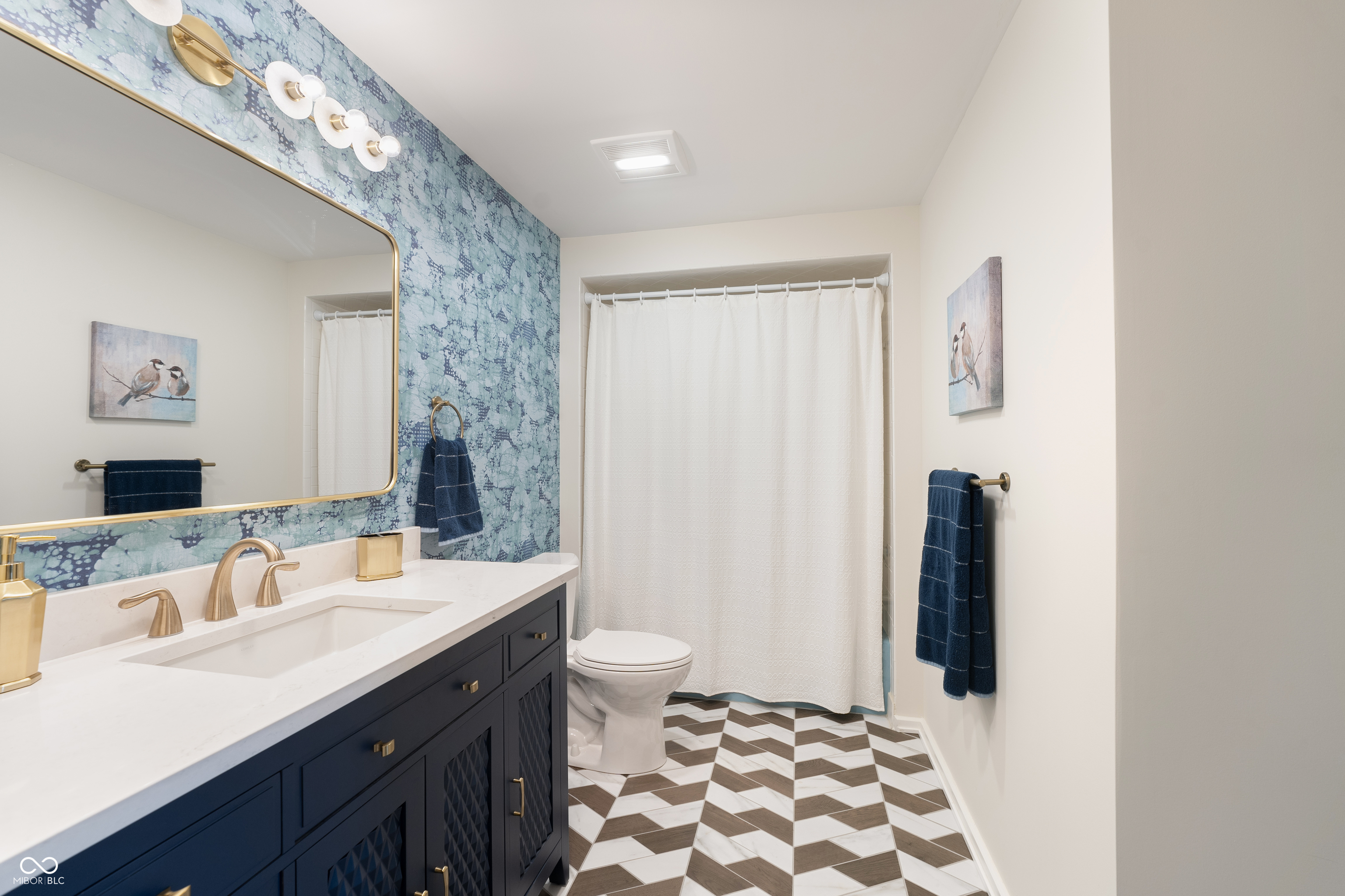 Bathroom with navy vanity, blue patterned wallpaper, and geometric brown-and-white tile floor.