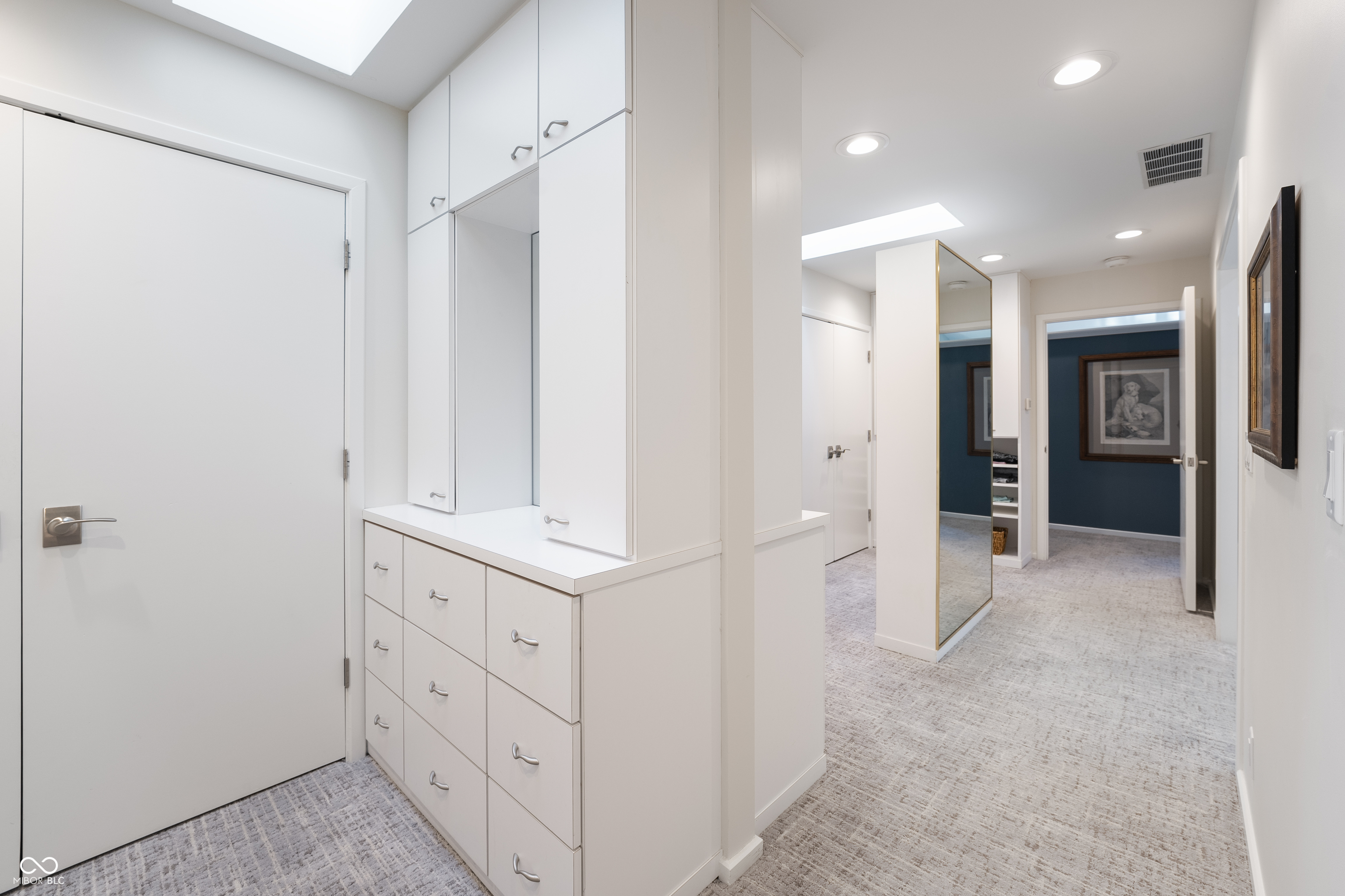 Walk-in closet with white built-in drawers, cabinets, and a full-length mirror.