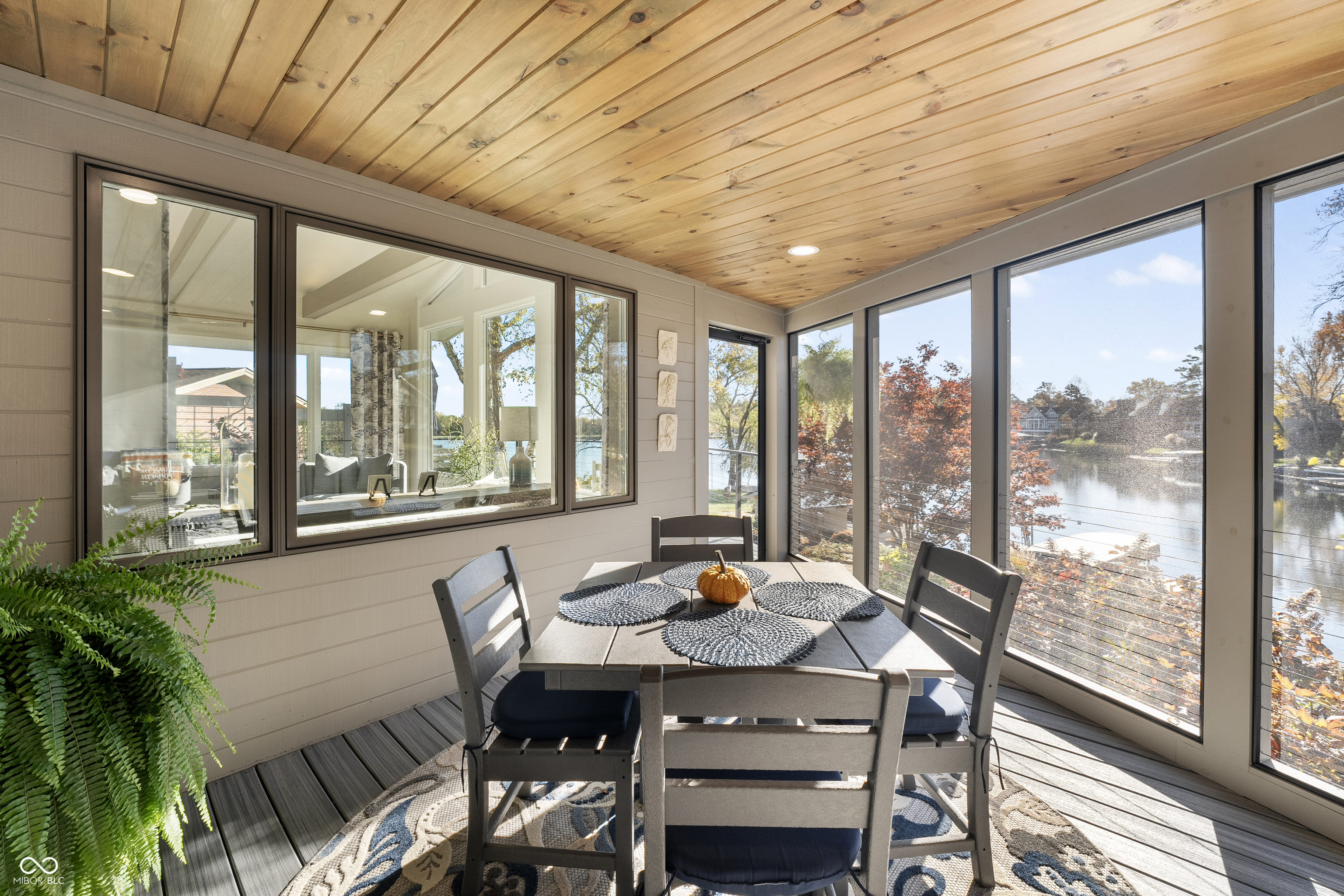 Enclosed dining porch with a wood ceiling, lake views, and autumn trees beyond the windows.