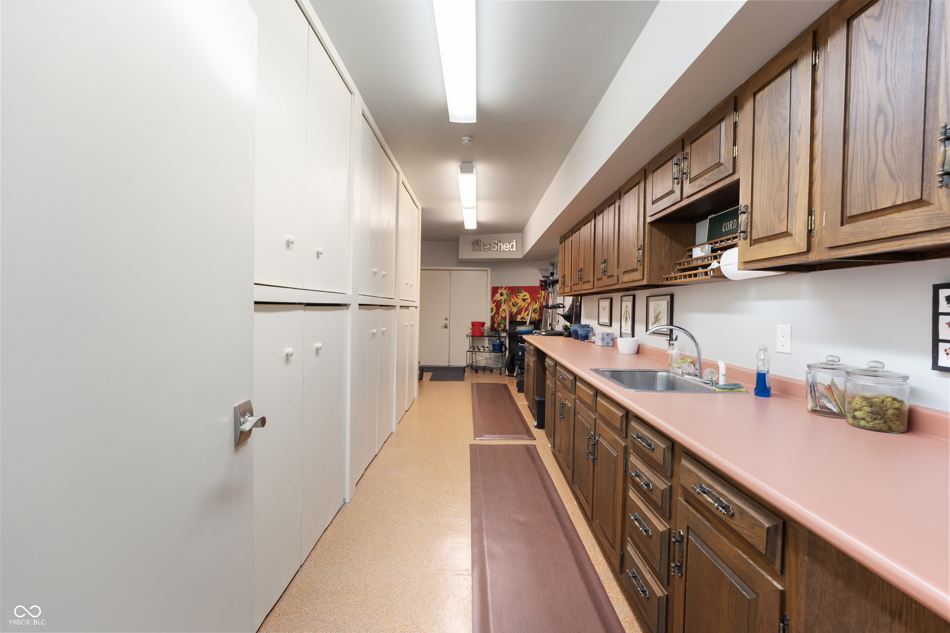 Utility room with extensive cabinetry, a pink countertop, and a stainless-steel sink.