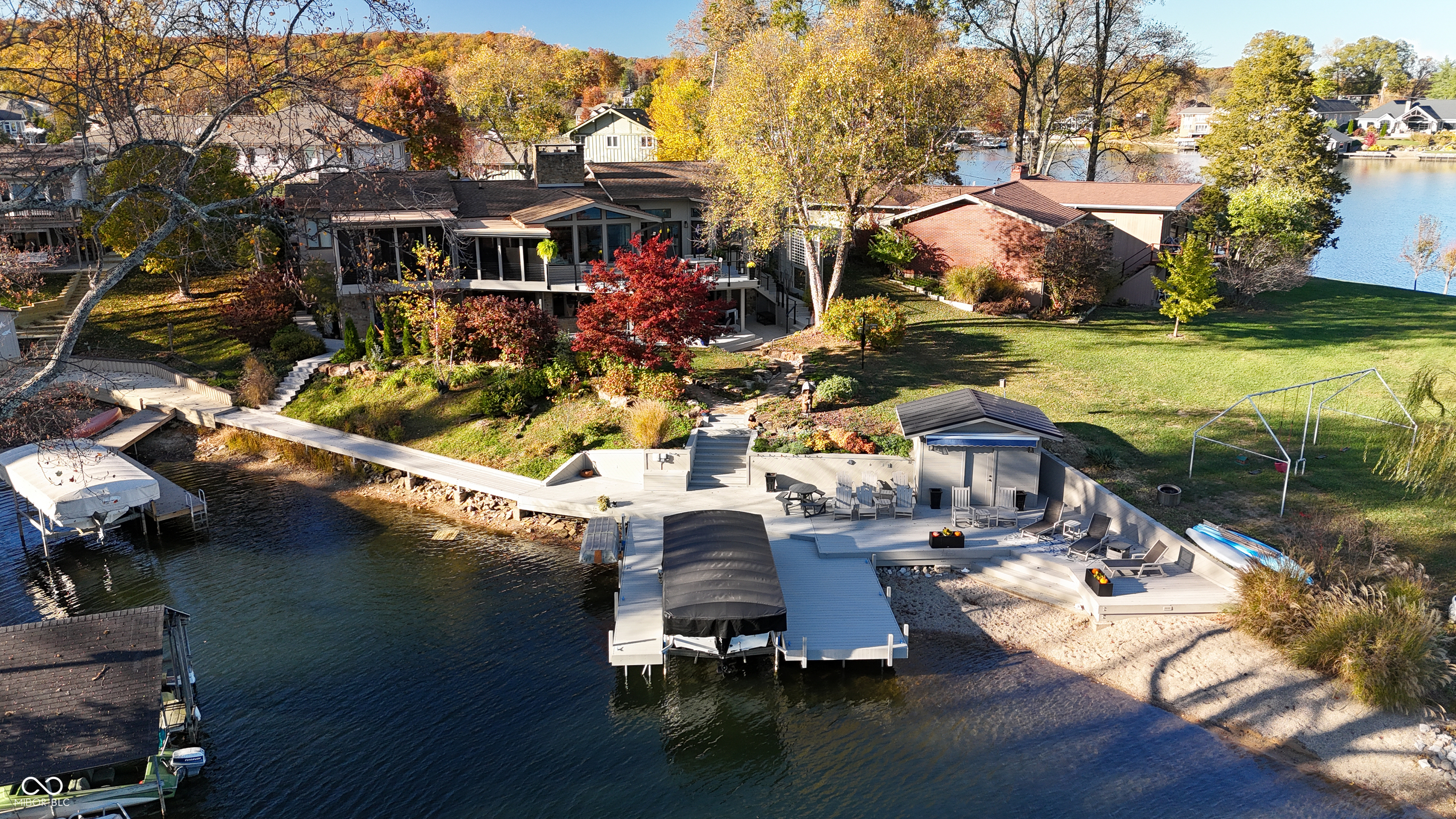 Aerial view of a lakefront home with a large dock, multi-level deck, and autumn foliage.