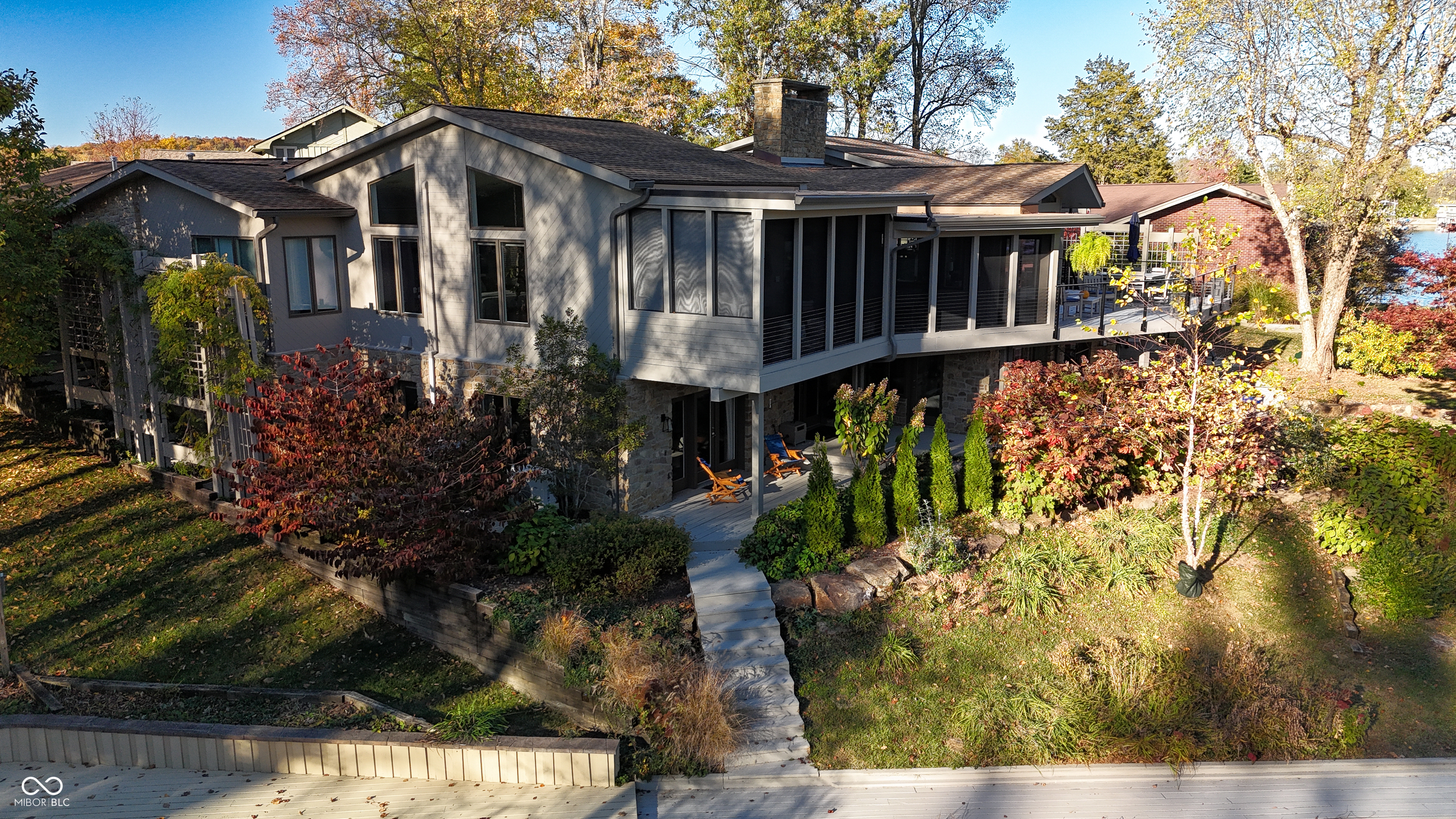 Modern gray home with a screened porch, stone accents, and autumn landscaping.