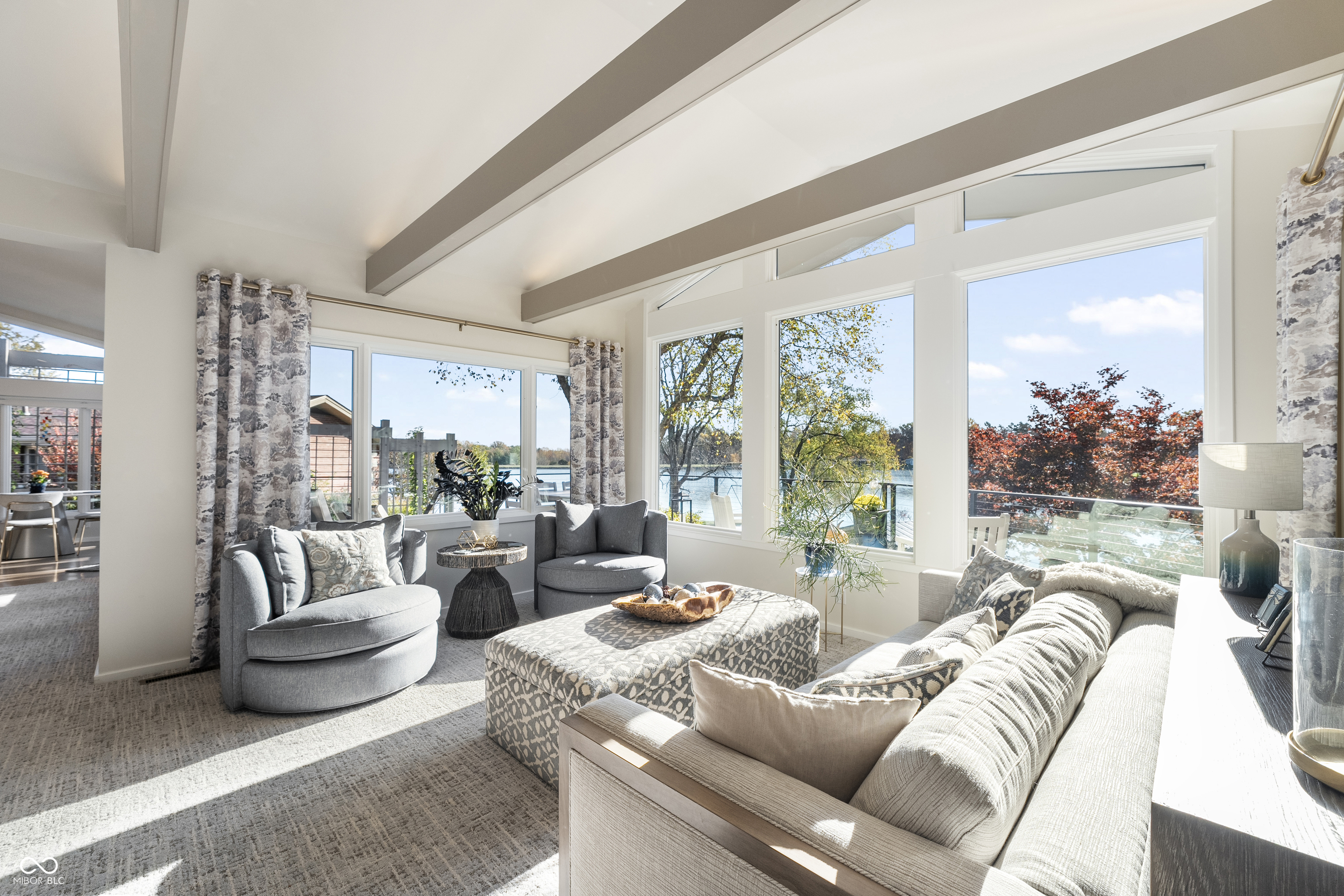 Furnished living room with vaulted beam ceiling and wide lake-view windows.