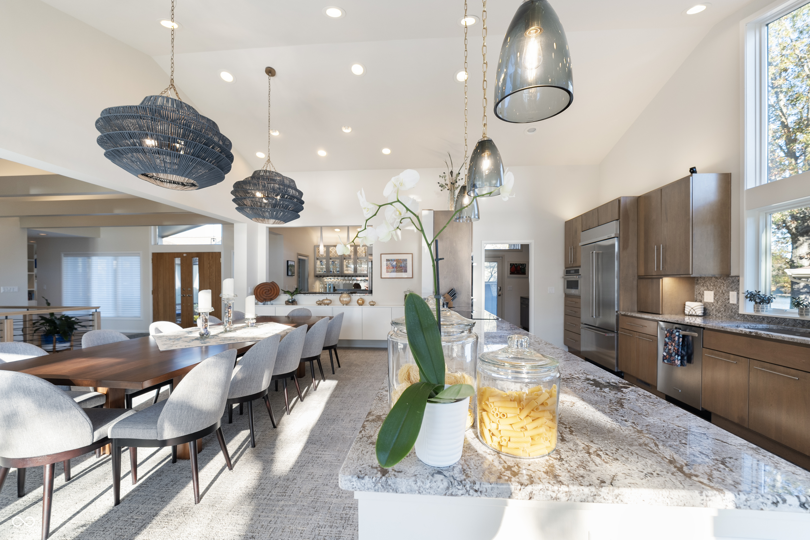 Open kitchen and dining area with a large stone island, wood cabinets, and woven pendant lights.