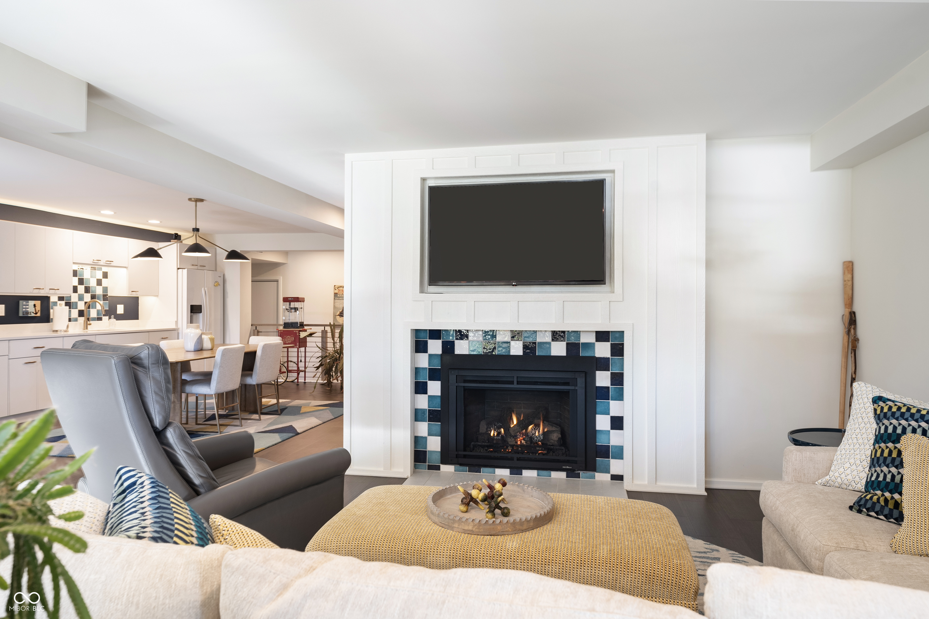 Living room with a blue-and-white tiled fireplace, wall-mounted TV, and open kitchen and dining area.