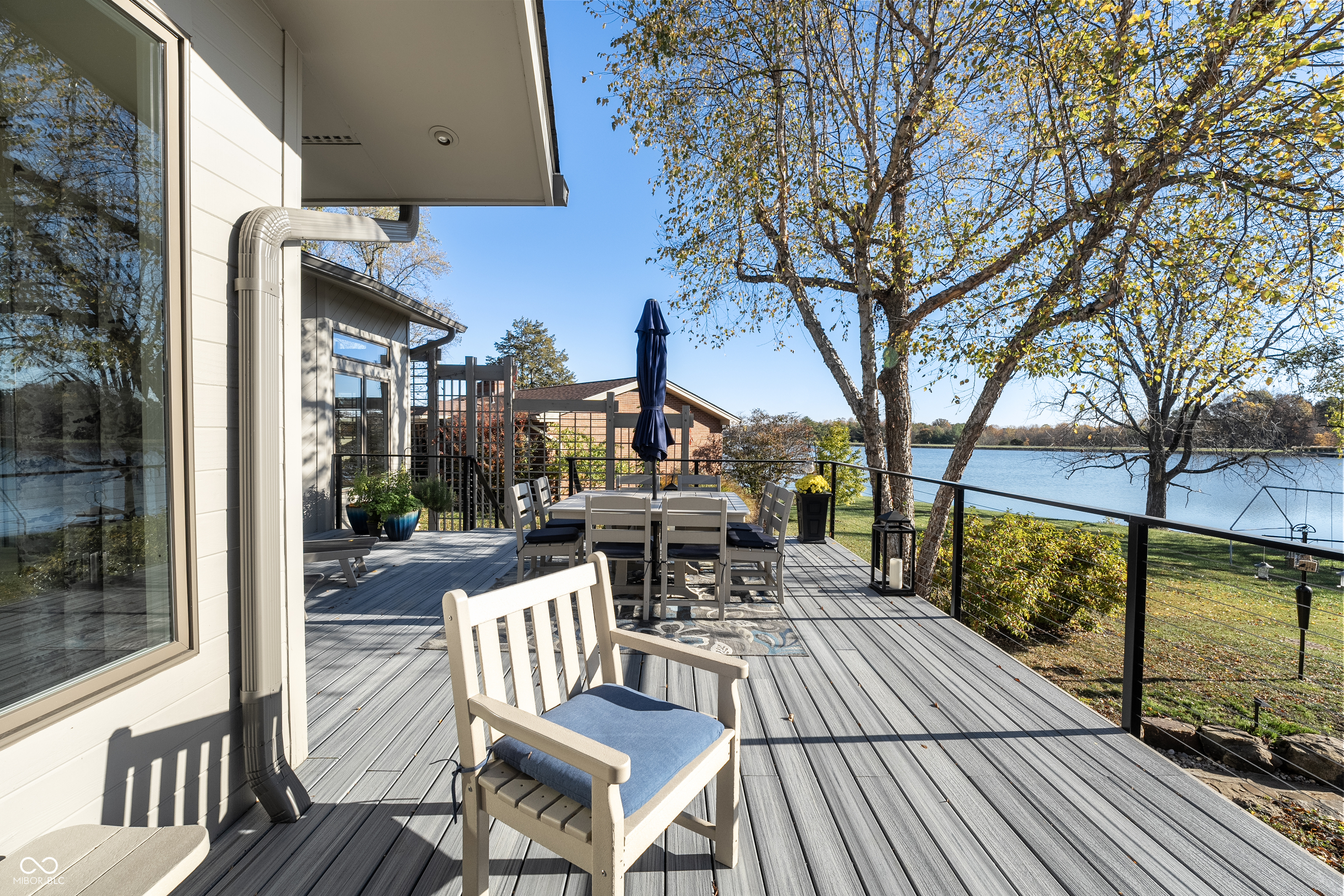 Furnished deck overlooking the lake, with dining set, gray decking, and autumn trees.