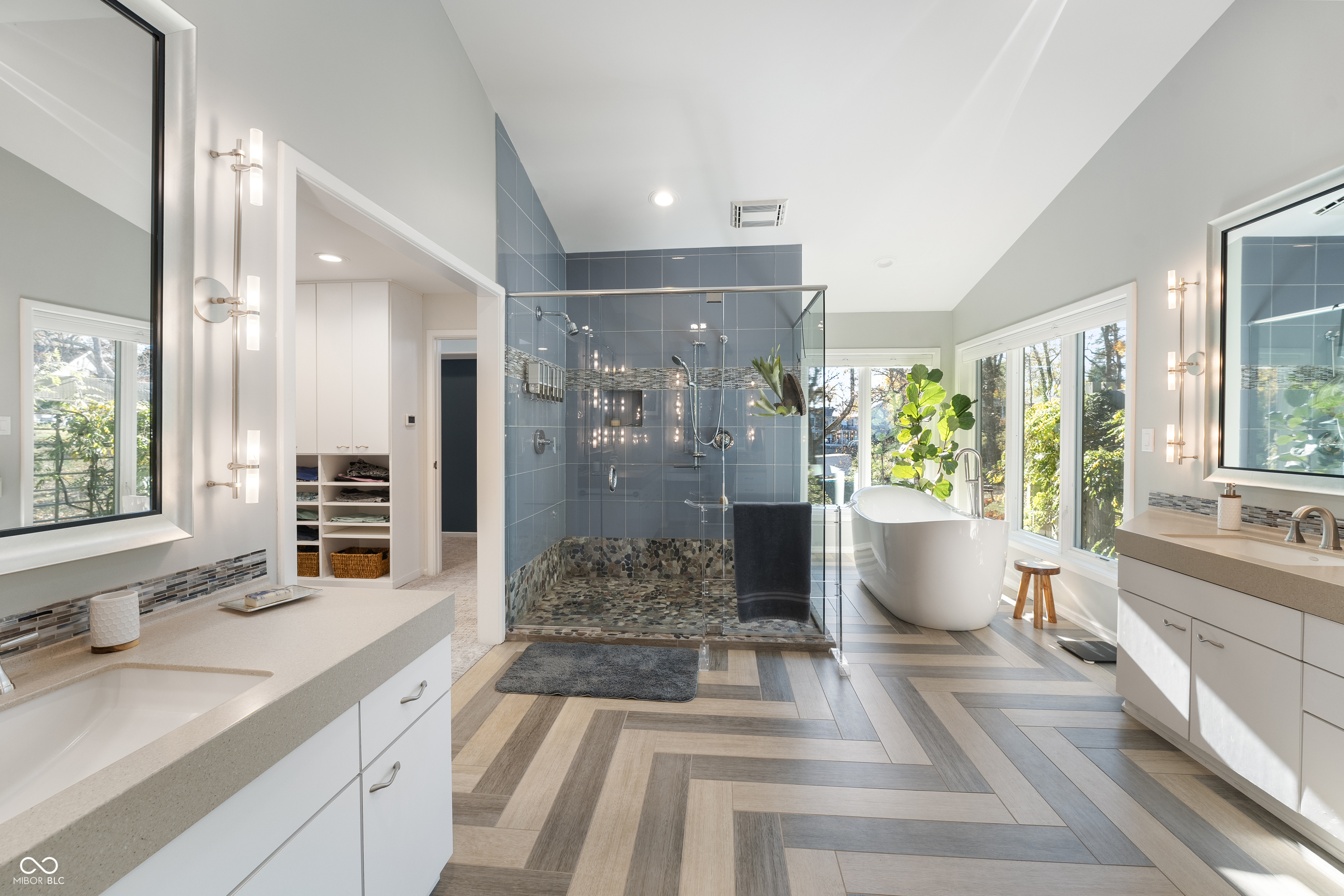 Contemporary bathroom with a blue-tiled glass shower, freestanding tub, and large windows.