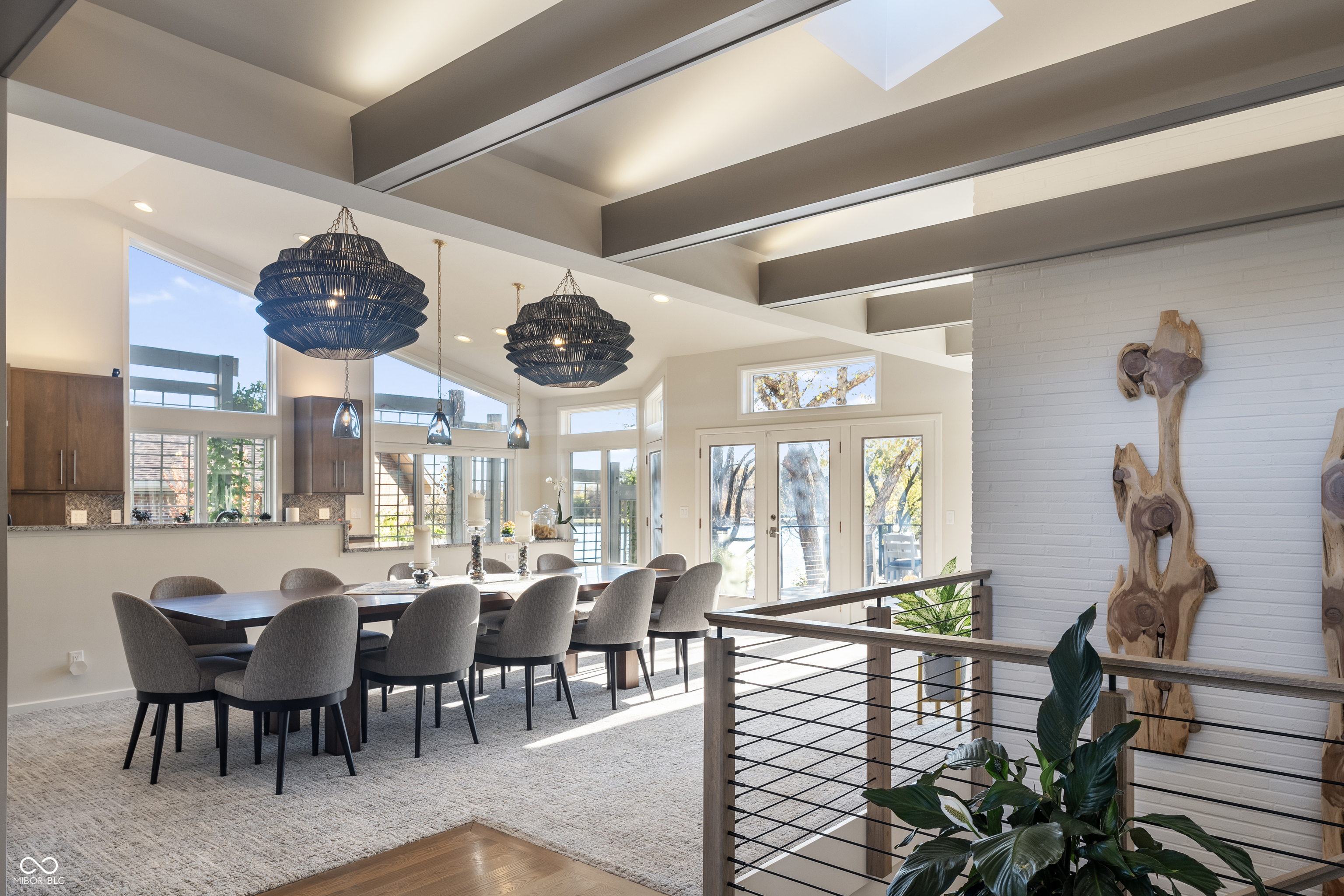 Dining area with sculptural pendant lights, exposed beams, and windows overlooking water.