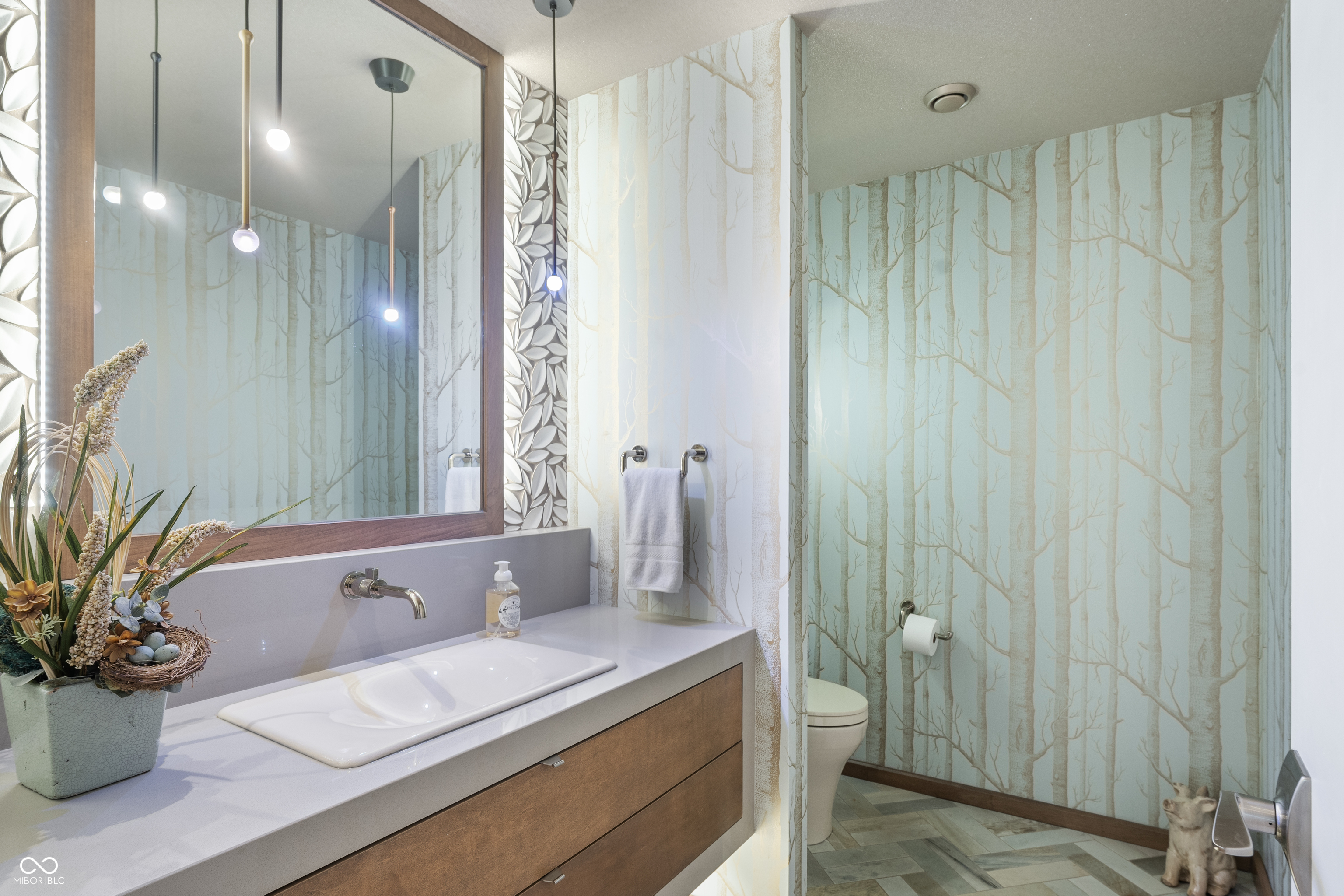 Modern bathroom with a floating wood vanity, white sink, and aqua tree-patterned wallpaper.
