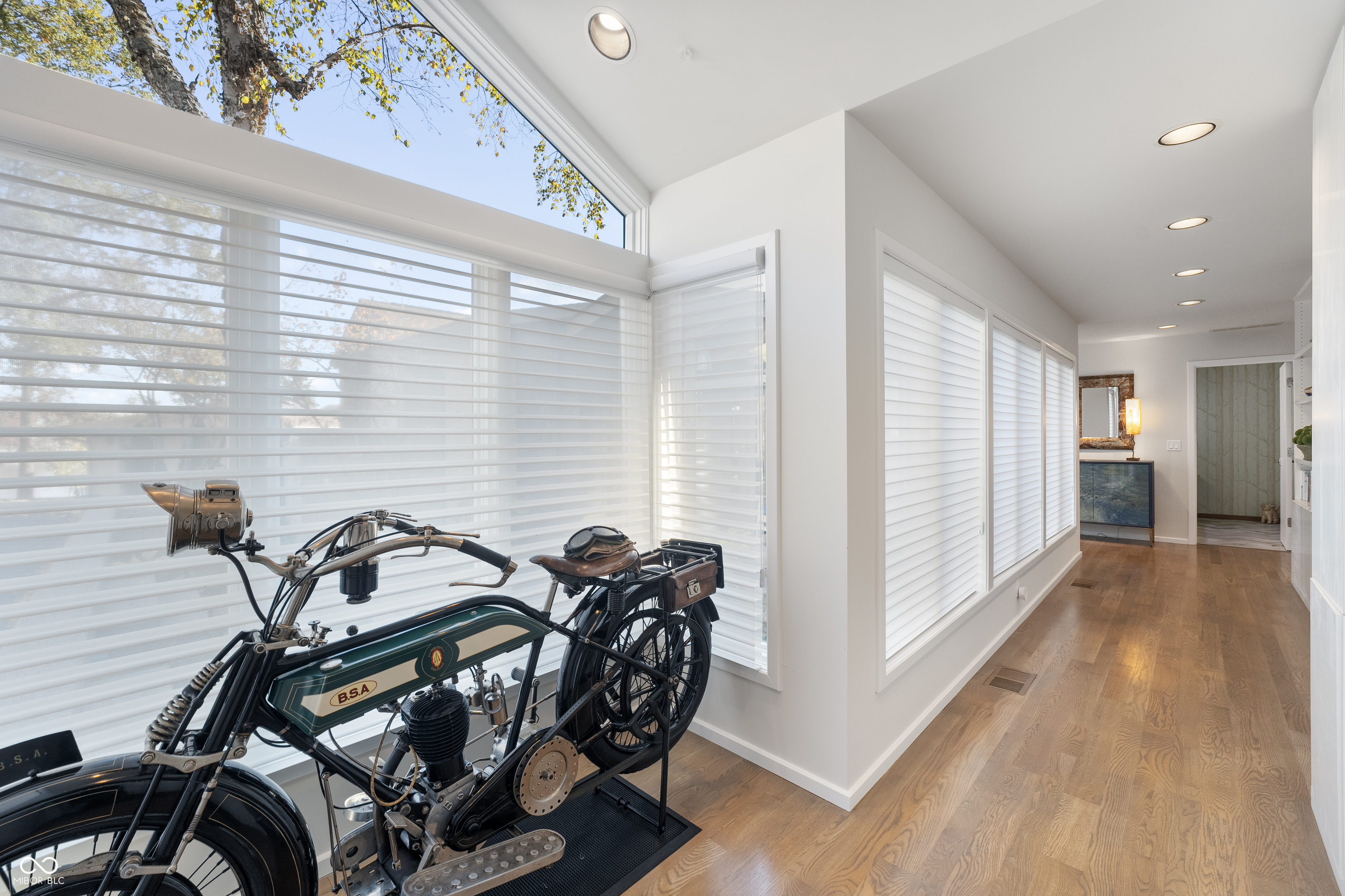Bright hallway with a vintage B.S.A. motorcycle displayed beside long windows with white blinds.