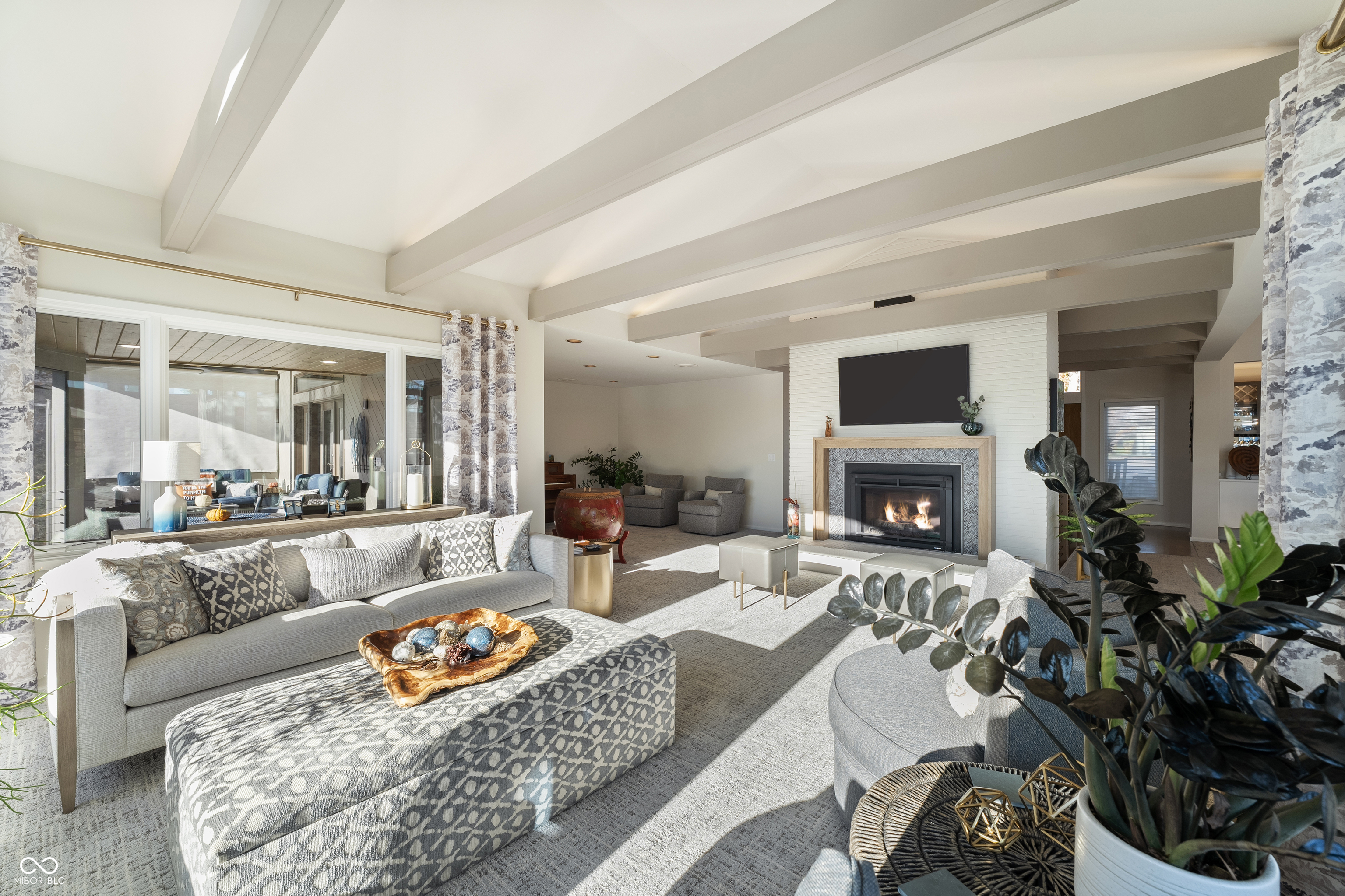 Living room with exposed beams, a lit fireplace, and a large sectional sofa beside patio windows.