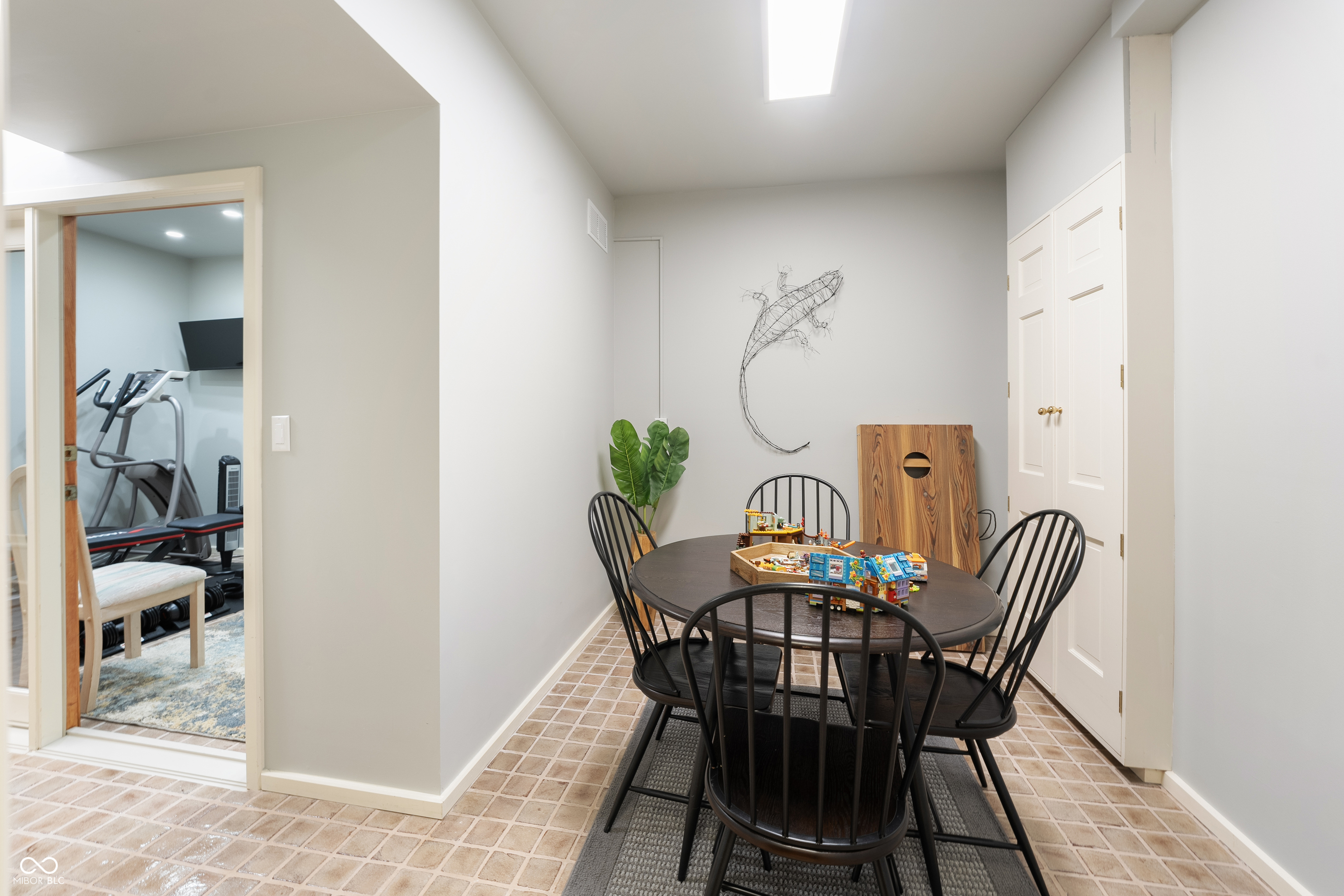 Recreation room with a toy-covered table, black chairs, and a doorway to a home gym.