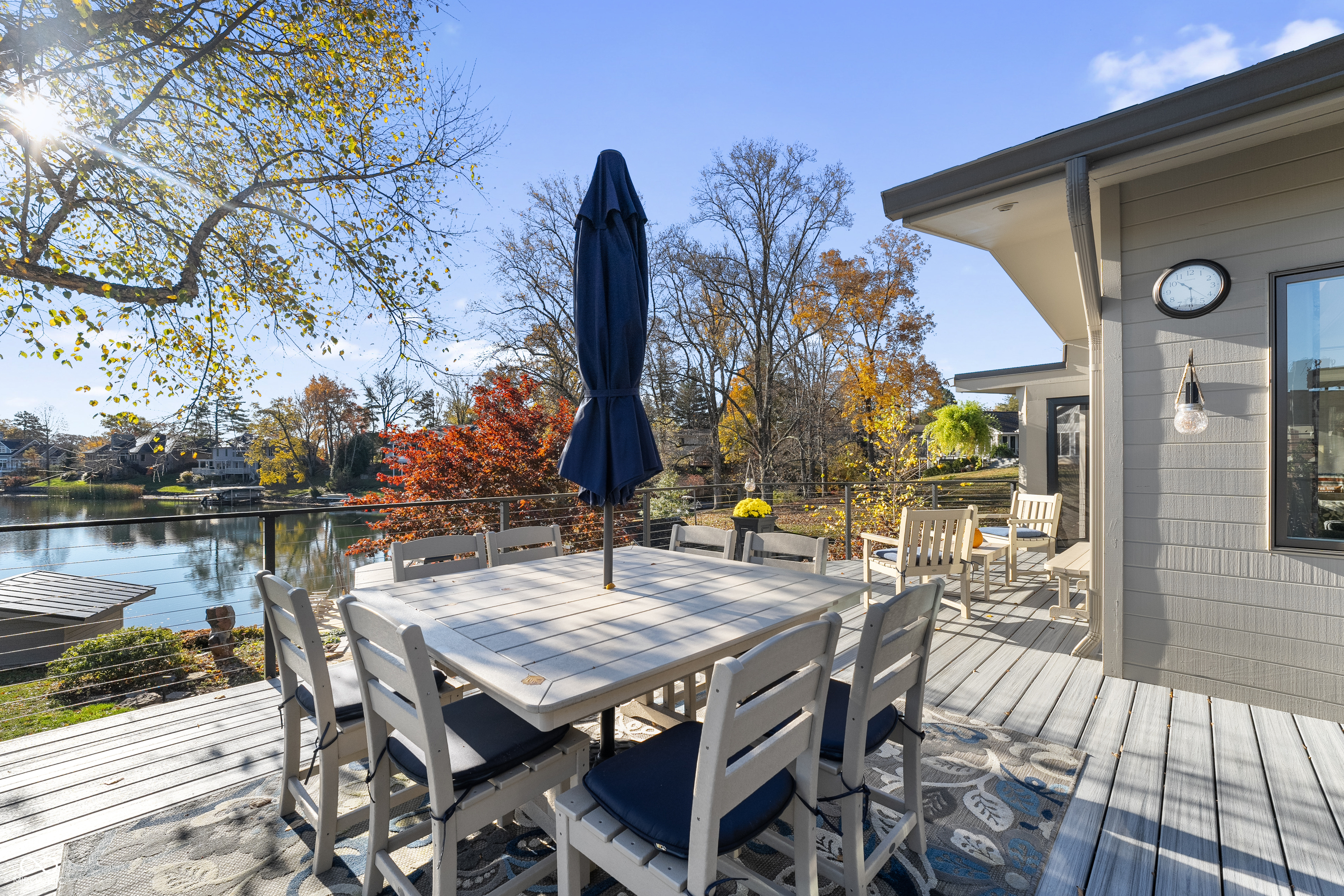 Furnished lakeside deck with dining table, closed umbrella, and autumn water view.