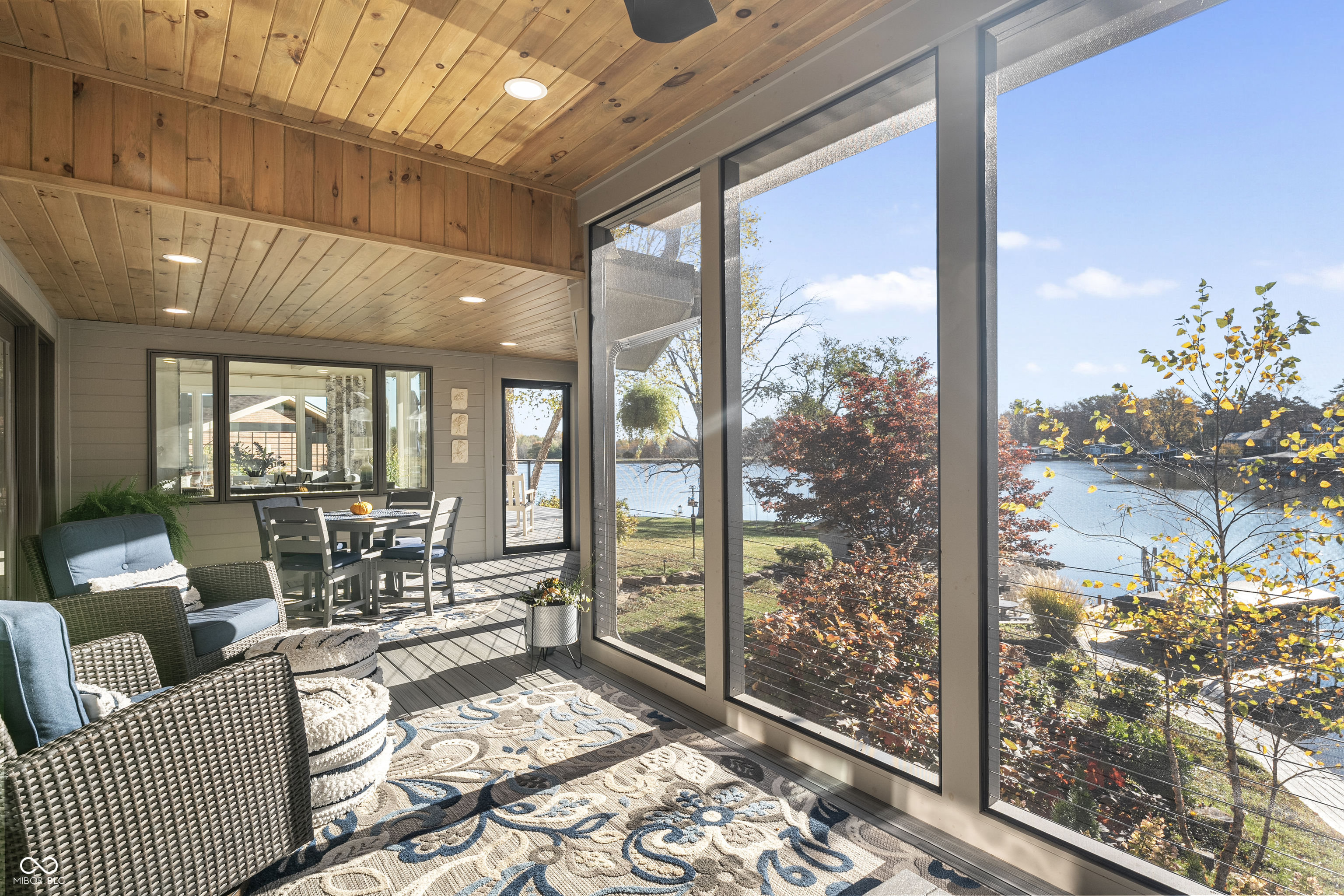 Furnished sunroom with a wood ceiling and floor-to-ceiling windows overlooking a lake.