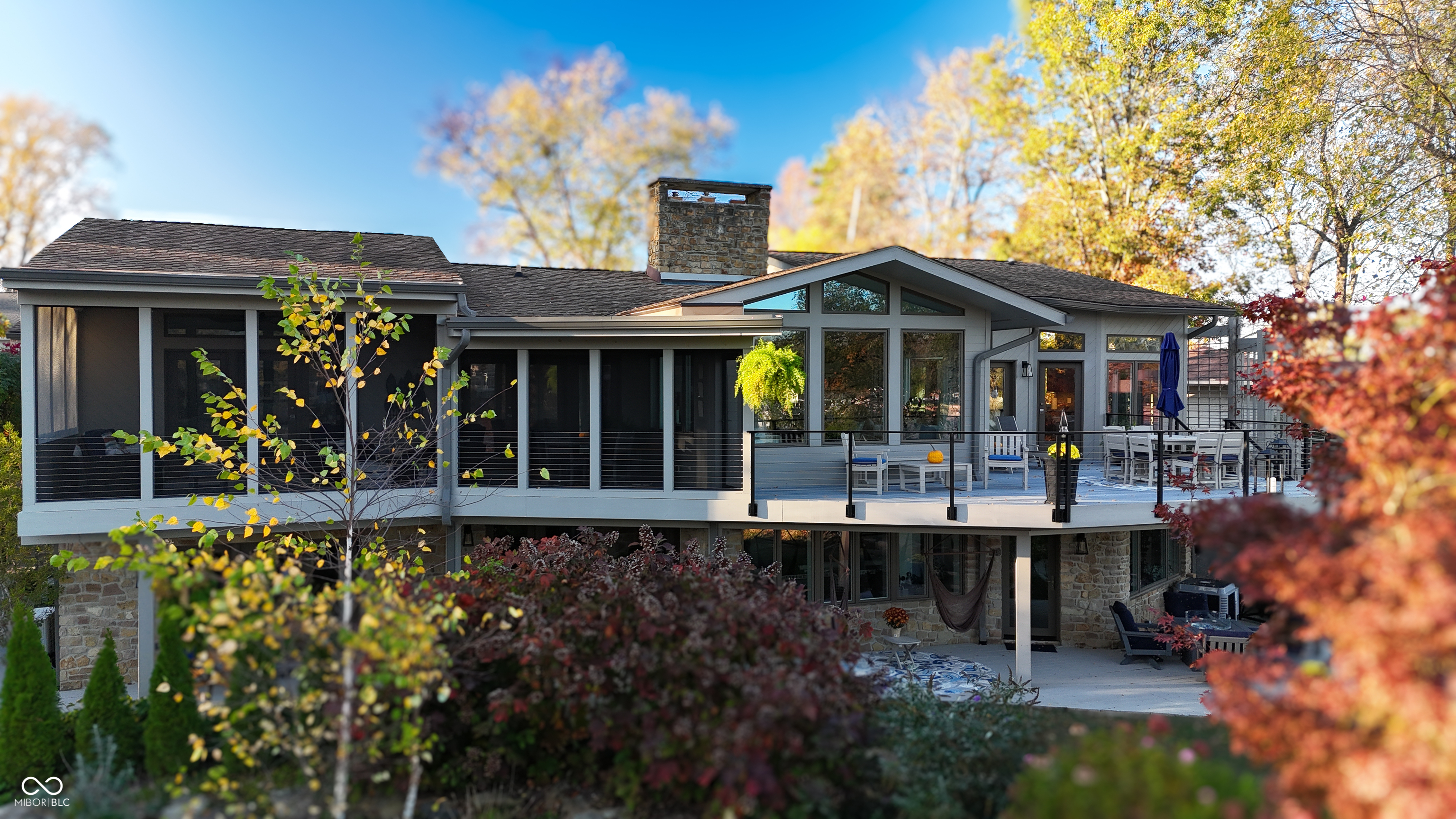 Modern home’s rear exterior with a raised deck, stone accents, and autumn foliage.