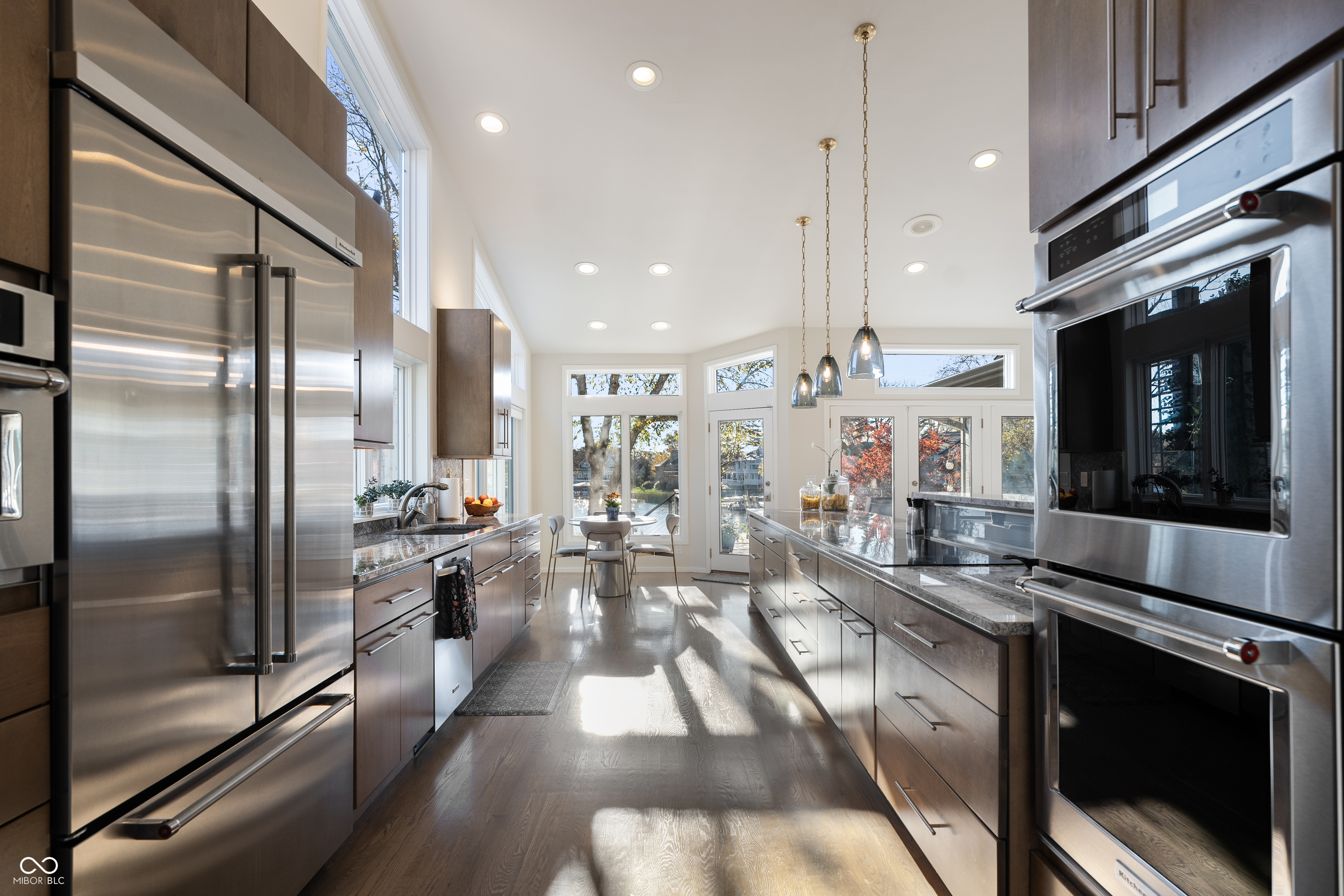 Modern kitchen with stainless steel appliances, dark cabinetry, and tall windows overlooking the water.