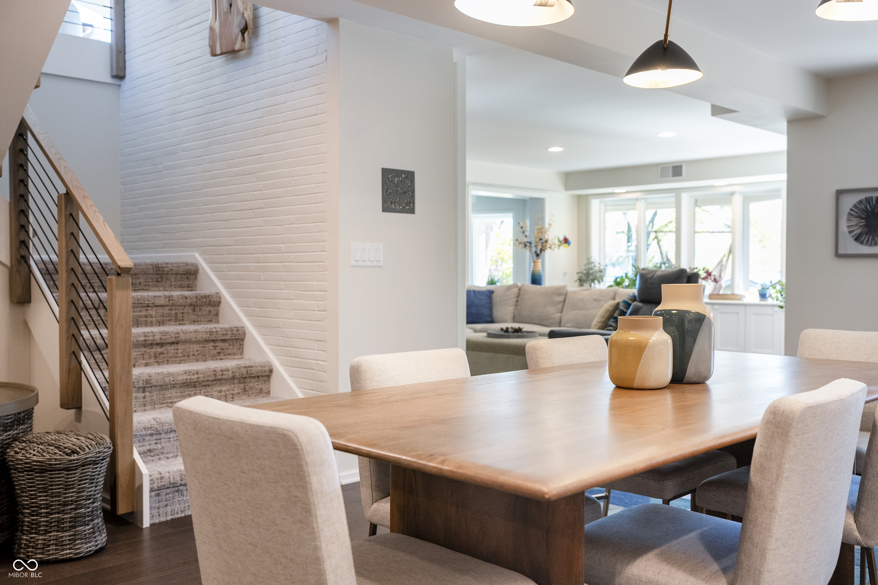 Dining area with a large wooden table, open living room, and carpeted staircase.