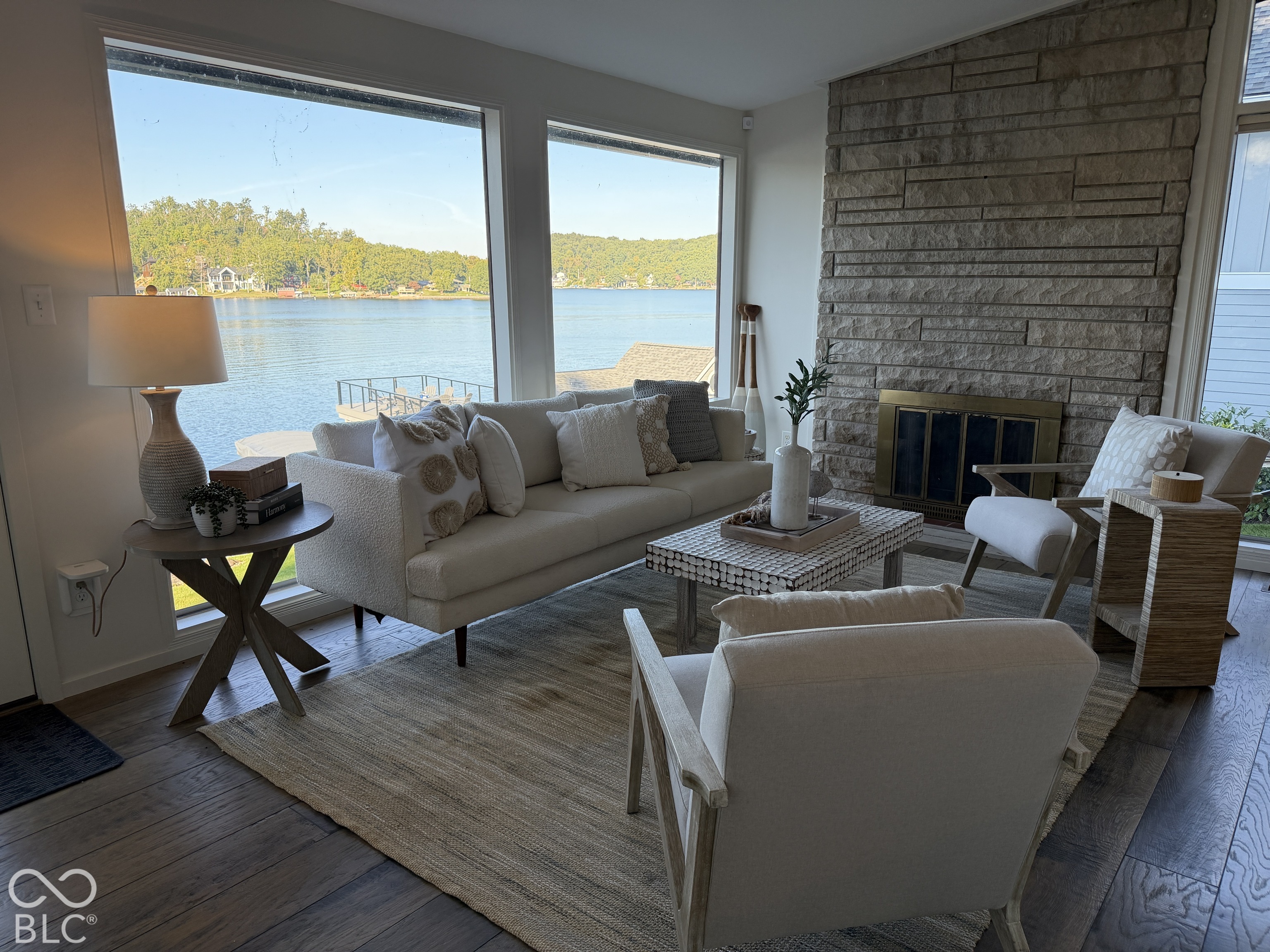 Lakefront living room with a stone fireplace and expansive windows overlooking the water.