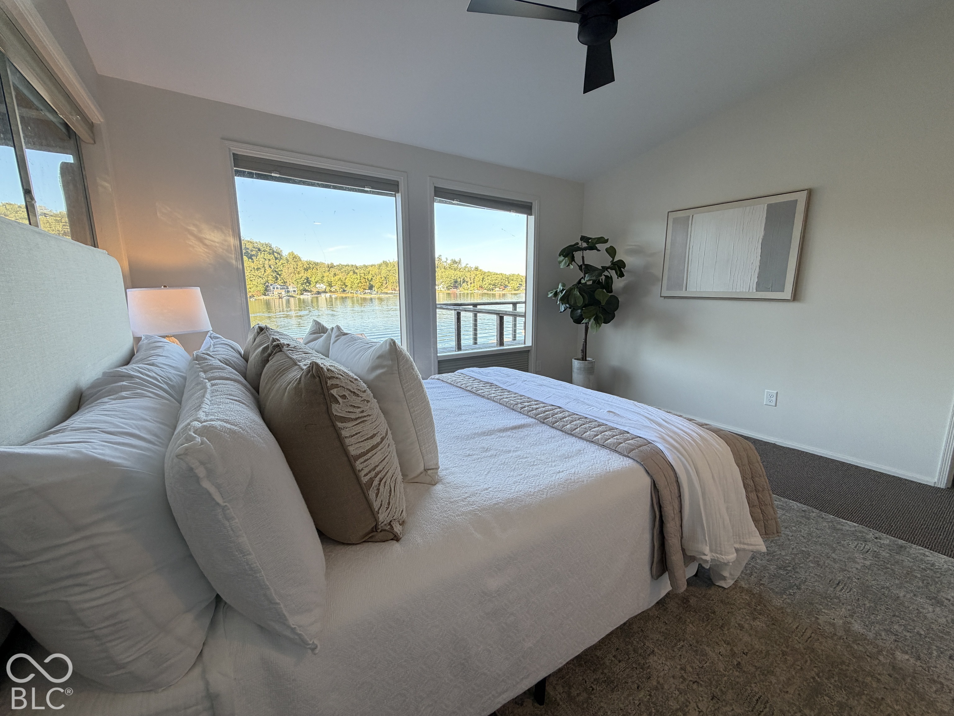 Staged bedroom with a large bed and wide windows overlooking a lake.