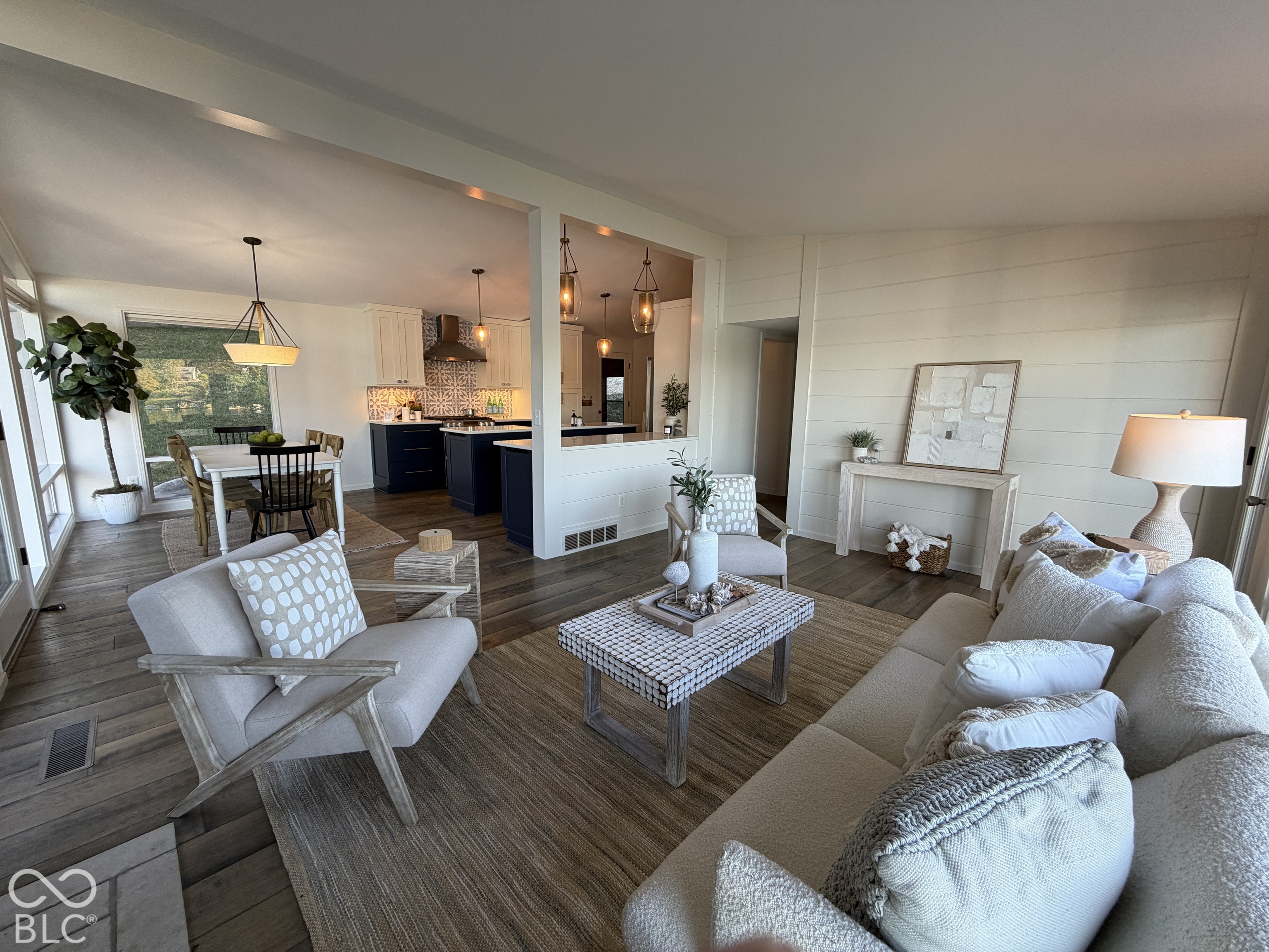 Open-plan living room with a furnished seating area, dining table, and navy-cabinet kitchen.