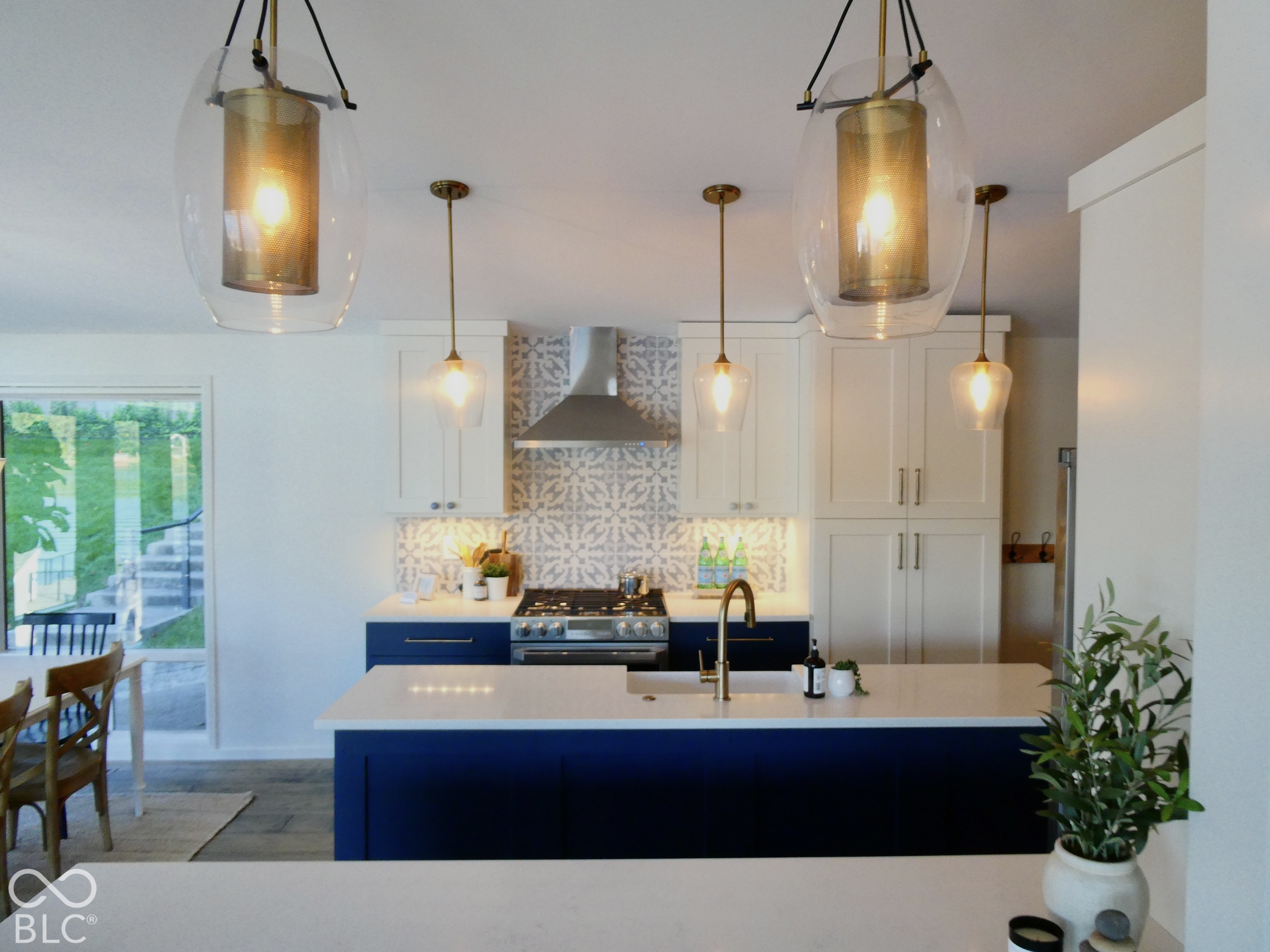 Kitchen with navy island, patterned backsplash, white cabinetry, and glass pendant lights.