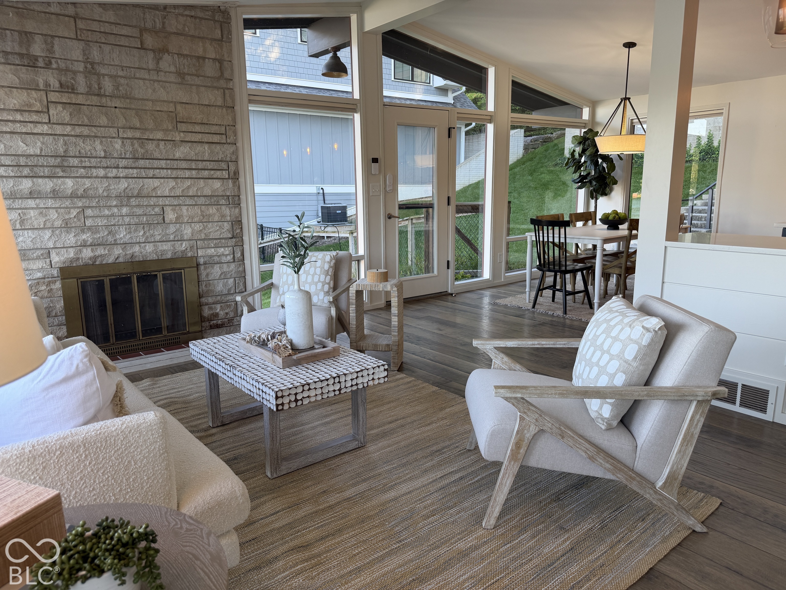 Living room with a stone fireplace, tall windows, and an adjoining dining area.